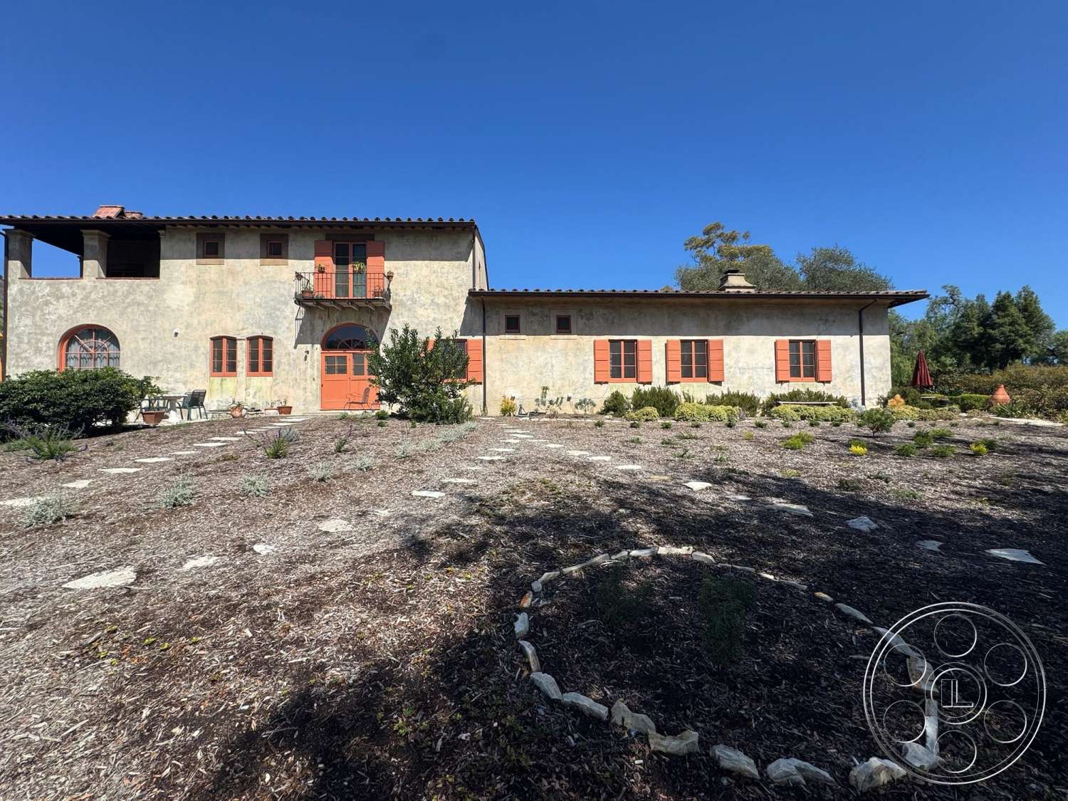 Farmstead Garden - exterior, landscaped garden, suburban setting, stucco walls, arched windows, gravel driveway, iron balcony railing, Mediterranean architectural style, red tiled roof, wooden window shutters, circular stone garden border