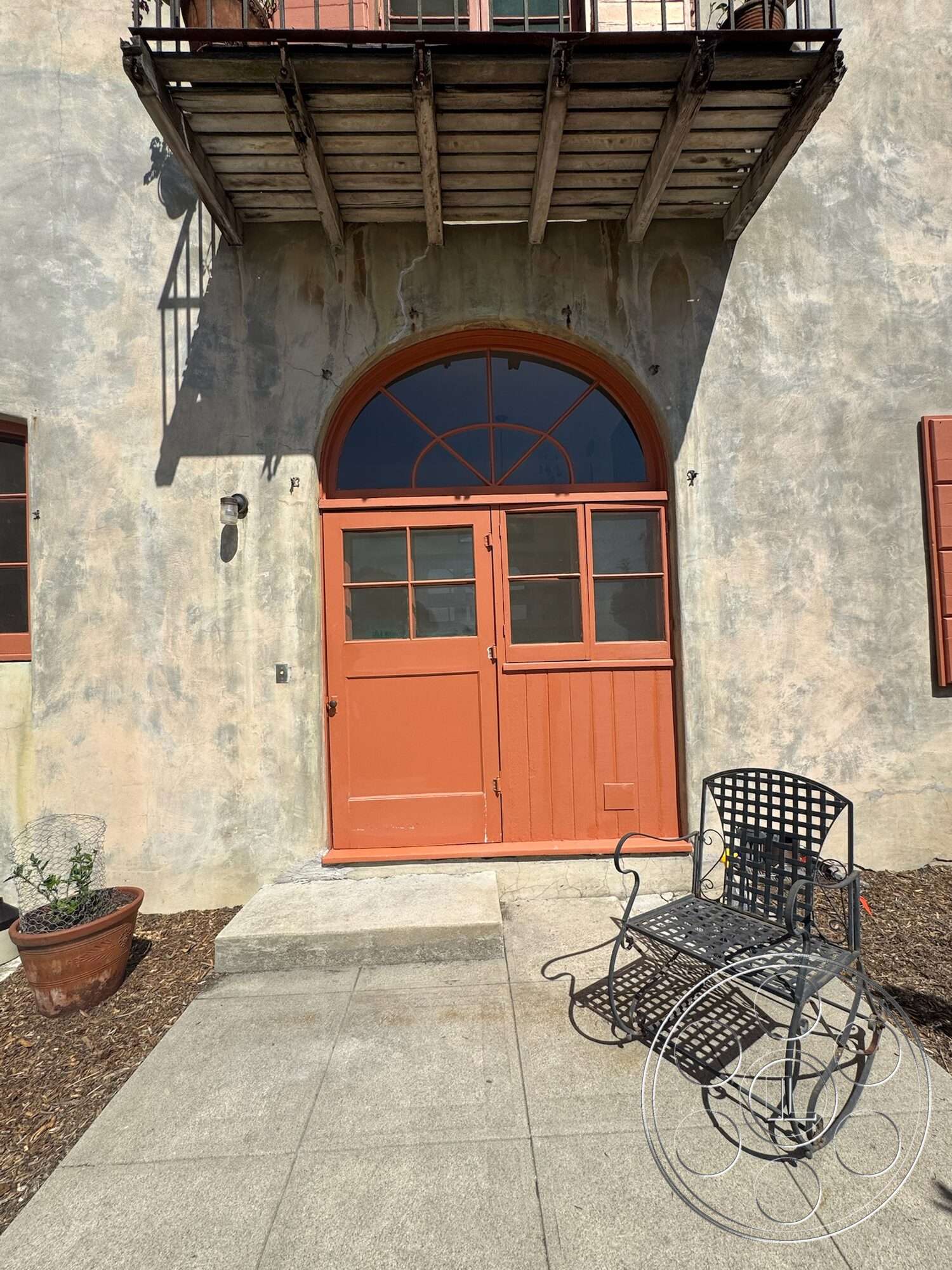 Farmstead Garden - exterior, rustic design elements, arched doorway, wooden window shutters, stucco wall finish, red wooden doors, wooden balcony, terra cotta planter, concrete step, gray concrete walkway, black wrought iron bench