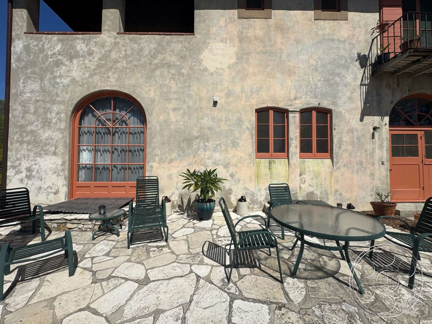 Farmstead Garden - exterior, rustic planters, decorative lanterns, arched windows, modern outdoor seating, plaster wall finish, potted plant accents, stone patio flooring, landscaped patio area, orange wooden window frames, green metal outdoor furniture, round glass top table