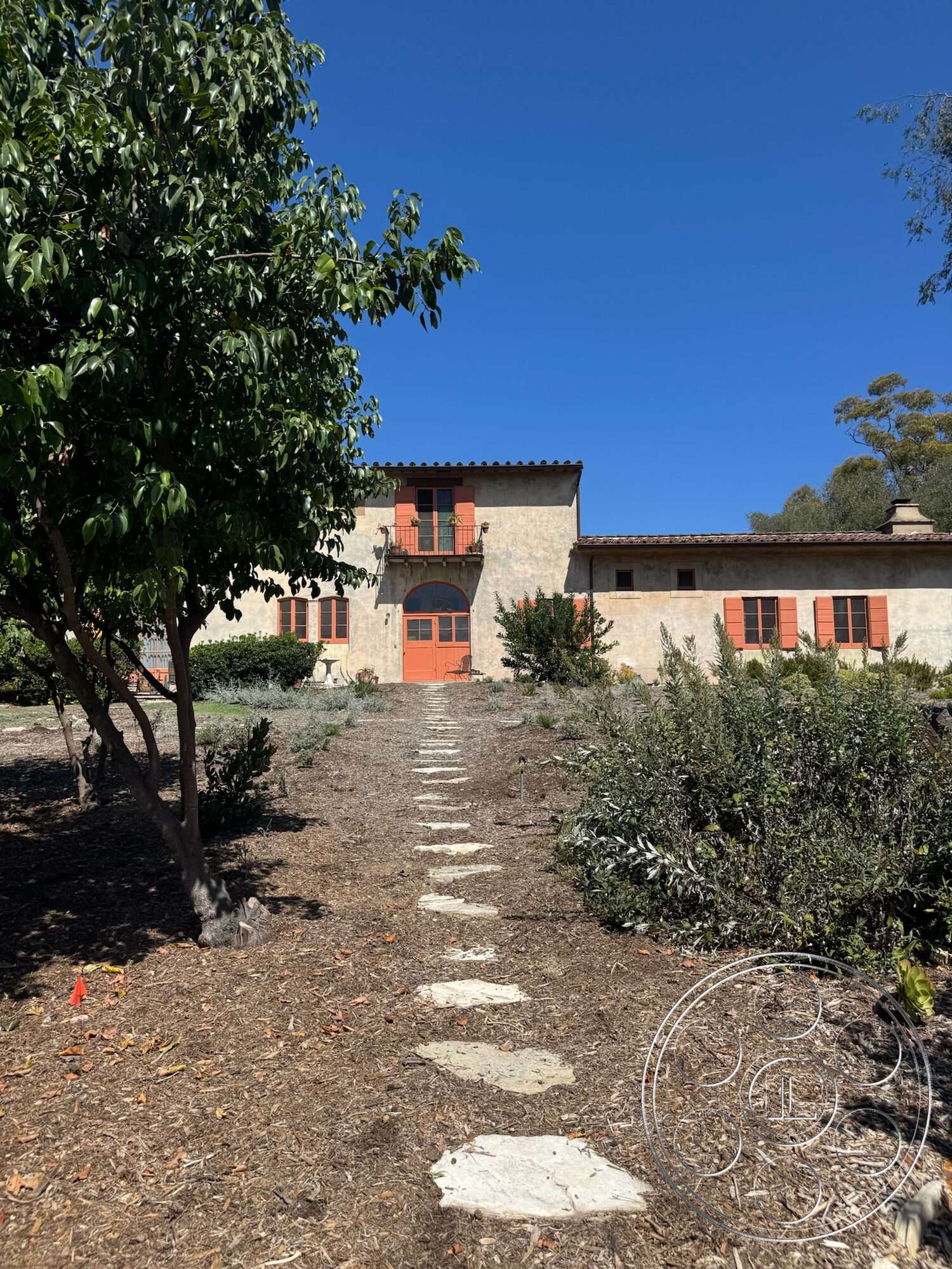 Farmstead Garden - stone pathway, arched doorways, red clay tile roof, double front doors, Mediterranean architectural style, sunny exterior, landscaped garden setting, stucco exterior walls, multi-story home, courtyard home design