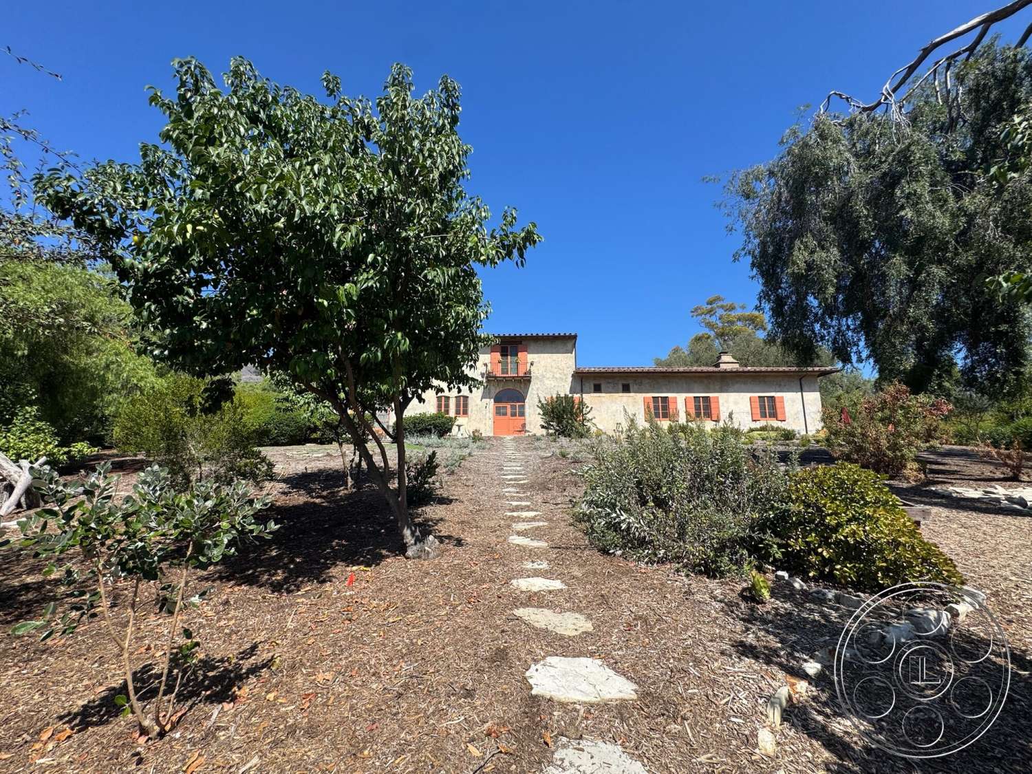Farmstead Garden - exterior, landscaped garden, natural greenery, single-story home, gabled roof, planted shrubs, outdoor setting, stone facade, Mediterranean architectural style, stepping stone pathway, wooden shutters, wooden entry door, gravel mulch ground cover