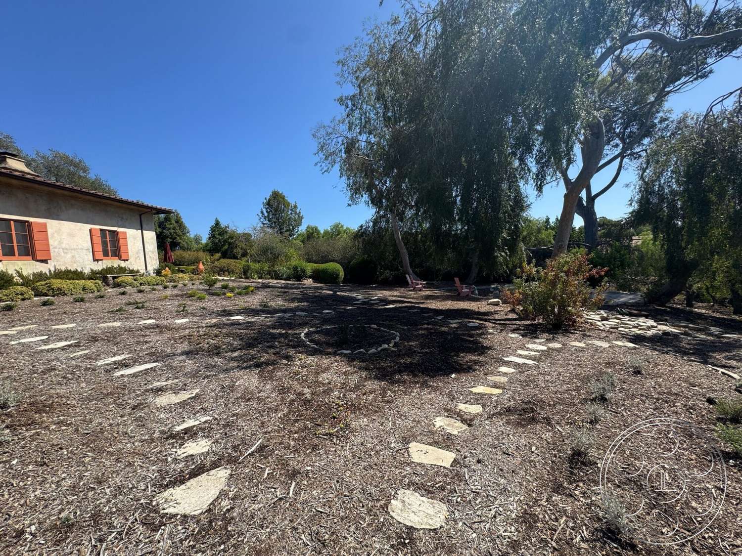 Farmstead Garden - decorative shrubs, residential home, stucco exterior walls, sunny outdoor environment, exterior garden setting, red wooden window shutters, stone pathway stones, mulch garden landscaping