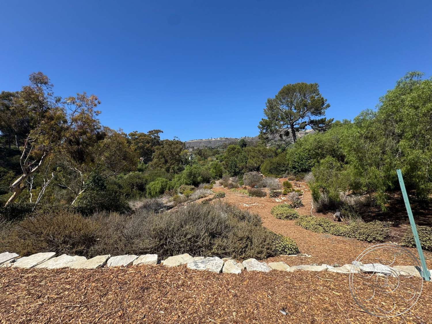 Farmstead Garden - exterior, natural stone elements, lush greenery, scenic hillside view, open sky, stone garden border, native plant landscaping, wood mulch ground cover, walking path through garden