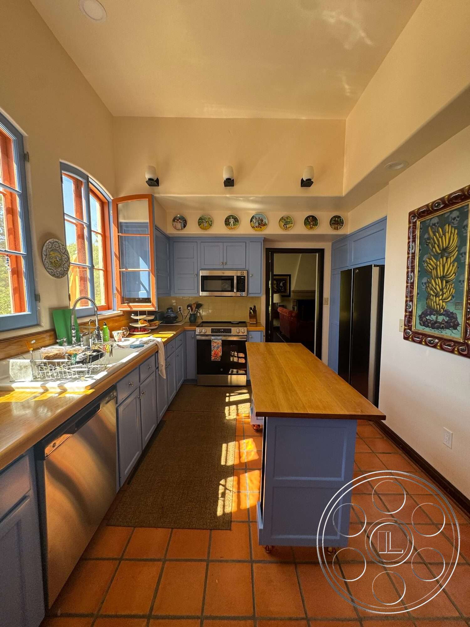 Farmstead Garden - stainless steel appliances, open concept layout, vaulted ceiling, textured plaster walls, terracotta tile flooring, blue cabinetry, light-filled space, interior kitchen, wood countertop island, large windows with wooden frames, dishwasher under counter, microwave integrated into cabinetry, decorative wall plates, rug under kitchen island