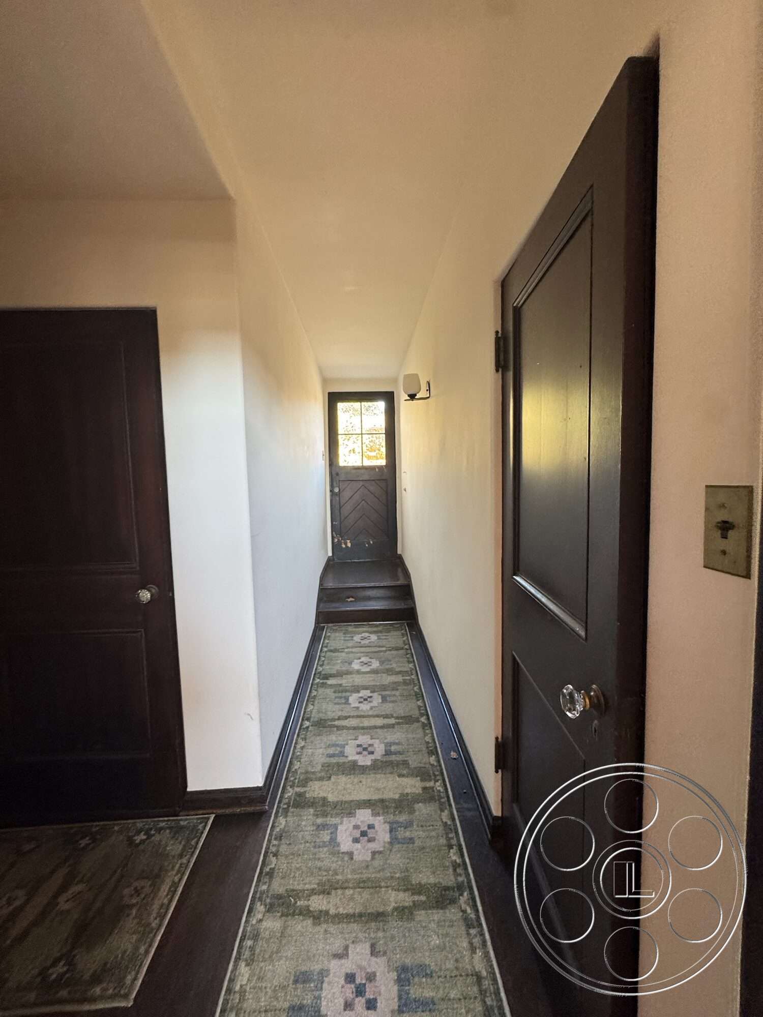 Farmstead Garden - decorative area rug, dark wood flooring, textured plaster walls, interior hallway, natural light entryway, dimensional wall sconces, wood panel doors, solid wood entrance door, chevron patterned door