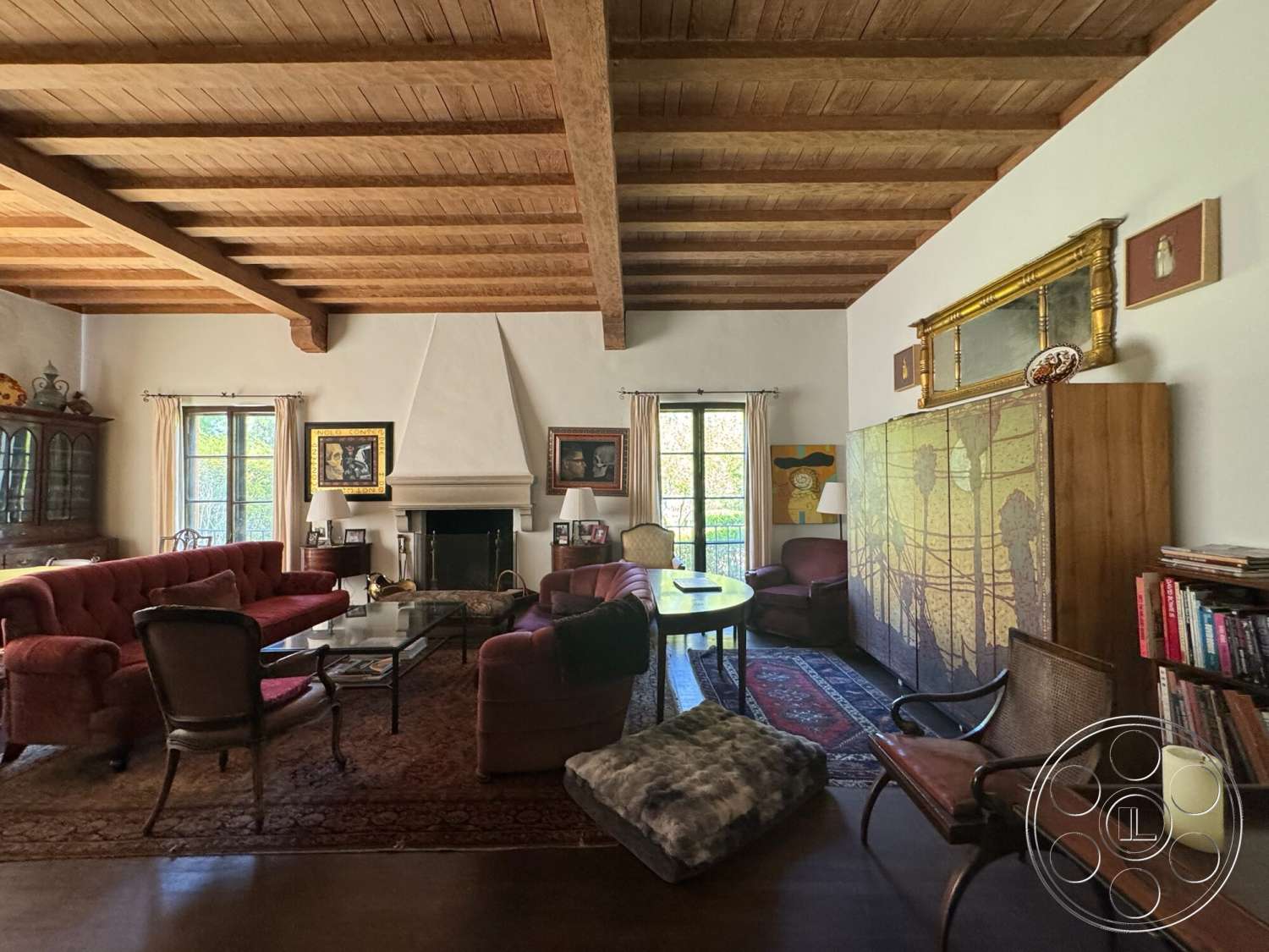 Farmstead Garden - large glass windows, textured plaster walls, open living space, comfortable seating area, tile floor, built-in bookshelves, exposed wood ceiling beams, vintage area rug, brick fireplace surround, neutral painted walls, wood beam ceiling, contemporary wall art, traditional wooden furniture, rustic coffee table, decorative gold-framed mirror
