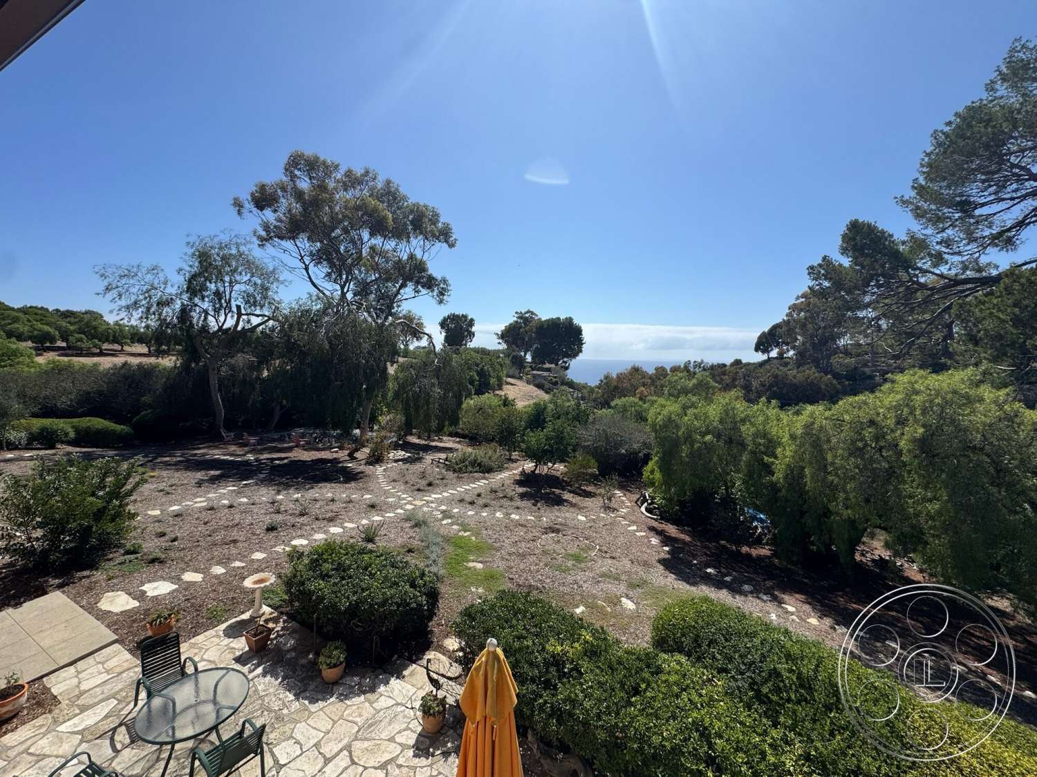 Farmstead Garden - exterior, ocean view, shade trees, hillside location, sunny outdoor setting, pathway stone pavers, stone patio flooring, green foliage landscaping, round table with metal chair set