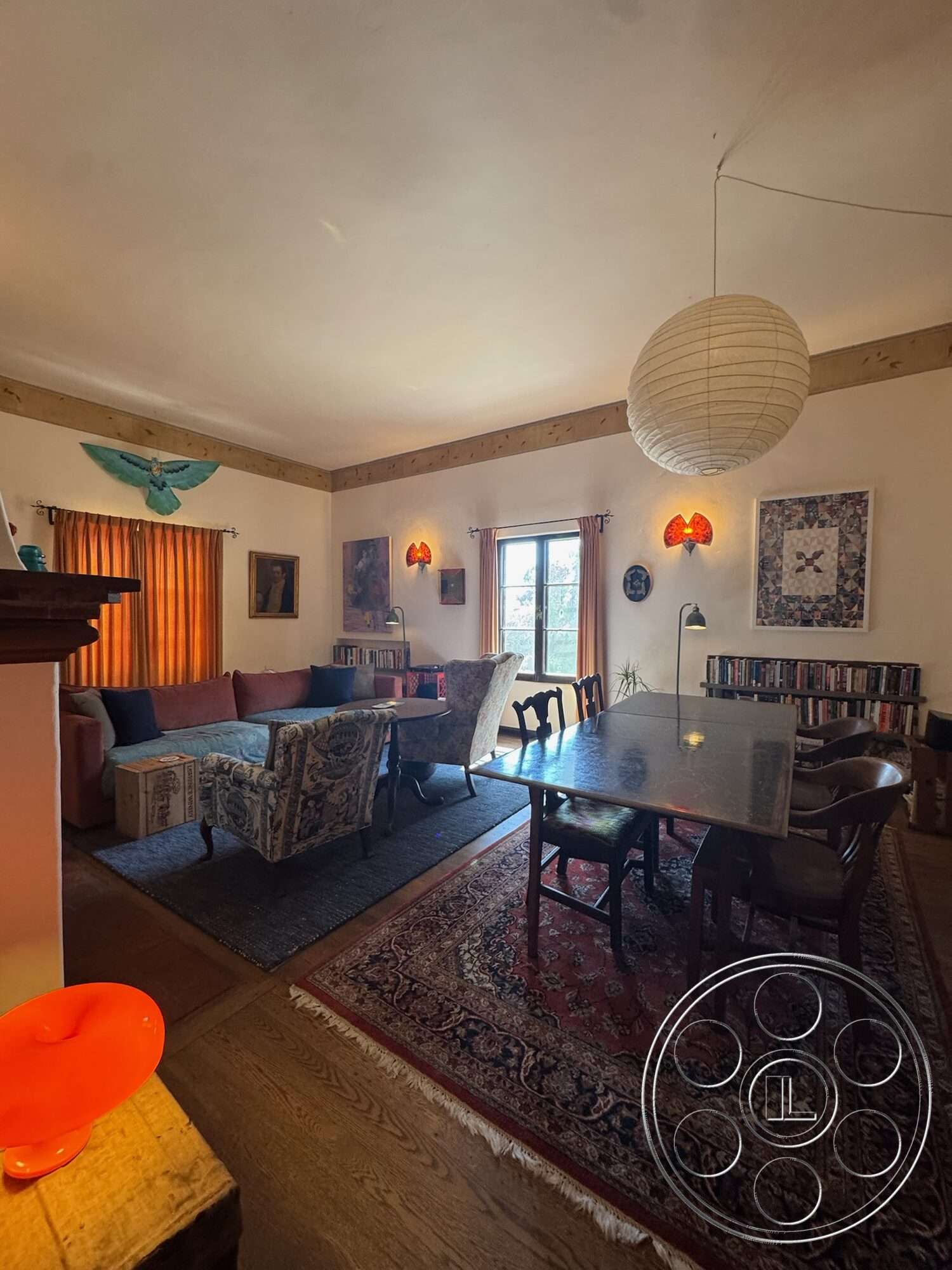 Farmstead Garden - upholstered dining chairs, colorful wall art, wooden dining table, floor-to-ceiling windows, wood floor, wooden bookshelf, exposed wood ceiling beams, vintage area rug, fabric upholstered sofa, curtains with orange hues, ceramic pendant light