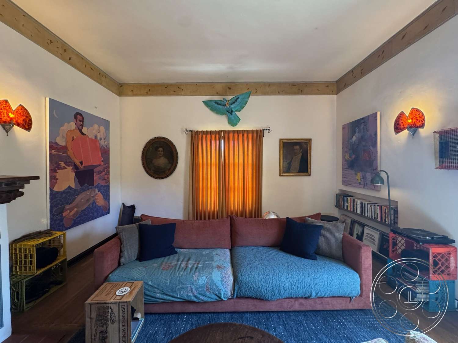 Farmstead Garden - wooden coffee table, colorful wall art, artwork on walls, plush sectional sofa, hardwood floor, framed portraits, decorative throw pillows, textured throw blankets, exposed wood ceiling beams, wood beam ceiling, orange sheer curtains, vintage wall sconces, open shelving with books, crate storage units, intricate light fixtures
