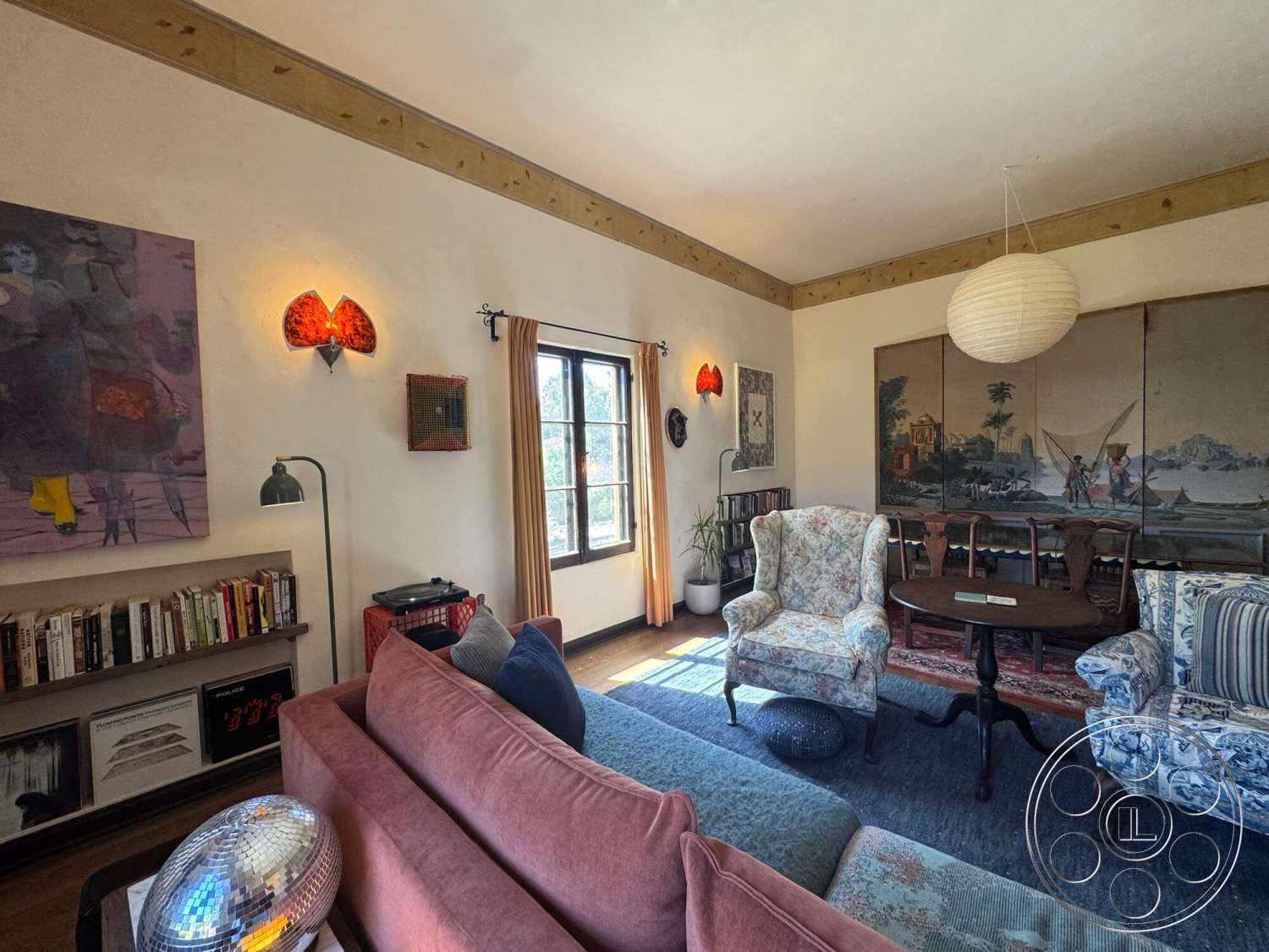Farmstead Garden - artistic wall art, sitting area, hardwood floor, textured plaster walls, green area rug, decorative light fixtures, decorative wall panels, round wooden dining table, wood beam ceiling, large window with curtain, floral upholstered chairs, retro-style pink sofa, vintage floor lamp, small bookshelf
