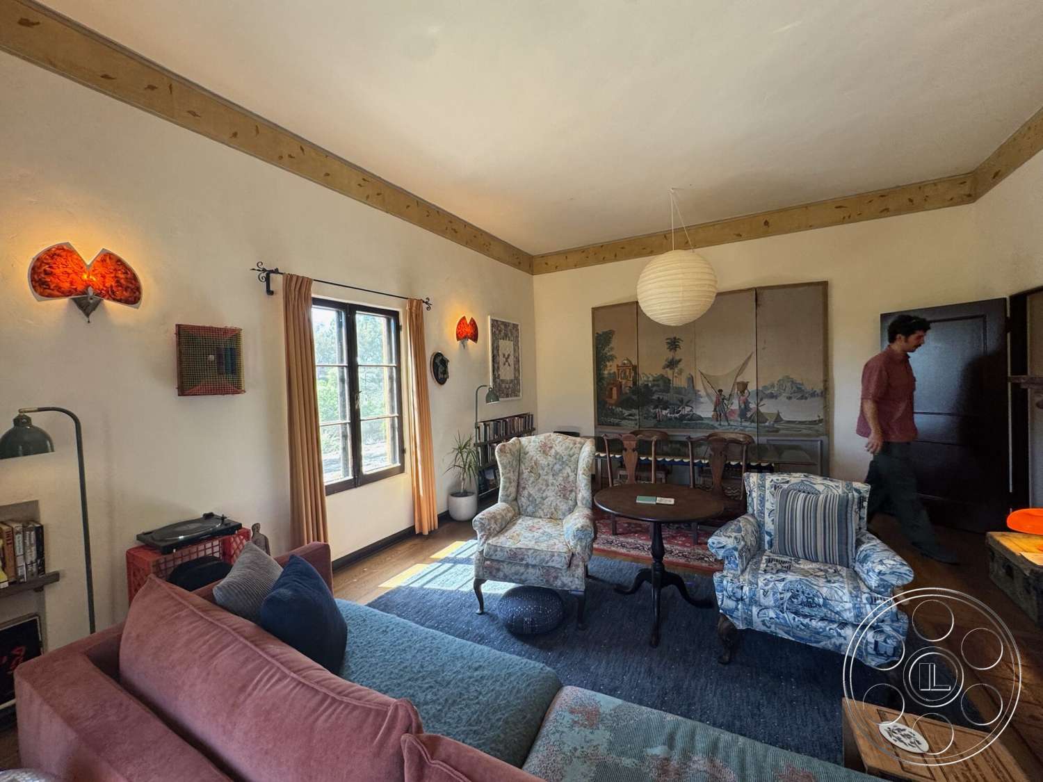 Farmstead Garden - decorative wall art, textured plaster walls, round wooden coffee table, exposed wood ceiling beams, hardwood living room floors, traditional wooden furniture, ceramic table lamp, curtained window treatment, pink velvet sofa, hanging paper lantern light fixture, blue floral upholstered chair