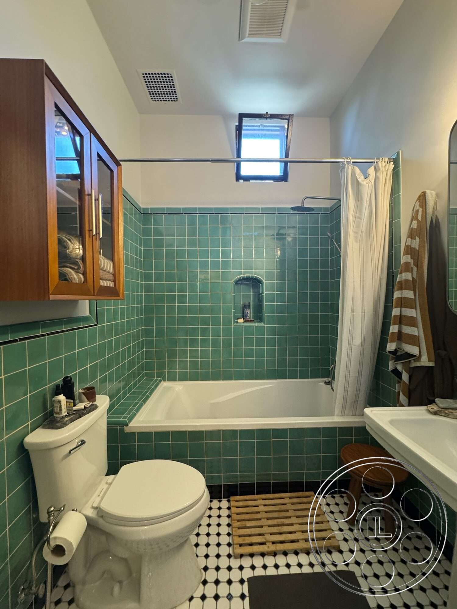 Farmstead Garden - white porcelain toilet, freestanding white bathtub, built-in niche for toiletries, round mirror above sink, black and white checkered tile flooring, window for natural light, wooden bath mat, turquoise glazed tile bathroom walls, walnut bathroom cabinet, glass shower curtain, neutral-colored towels hanging, single vanity with sink