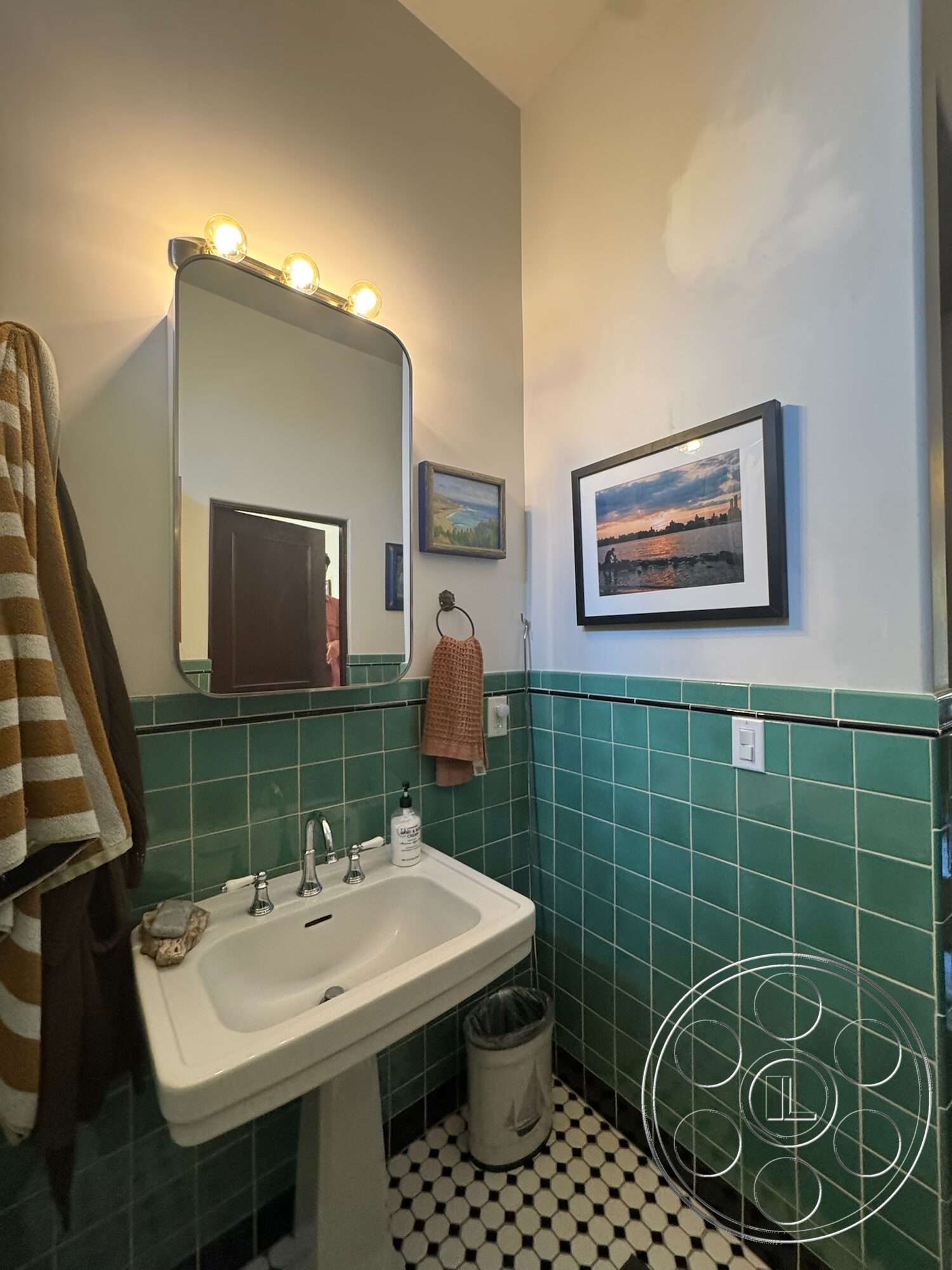 Farmstead Garden - framed wall art, textured plaster wall, striped towel hanging, pedestal sink with chrome fixtures, green ceramic tile bathroom walls, black and white hexagonal tile flooring, vanity mirror with light fixtures, decorative towel hook