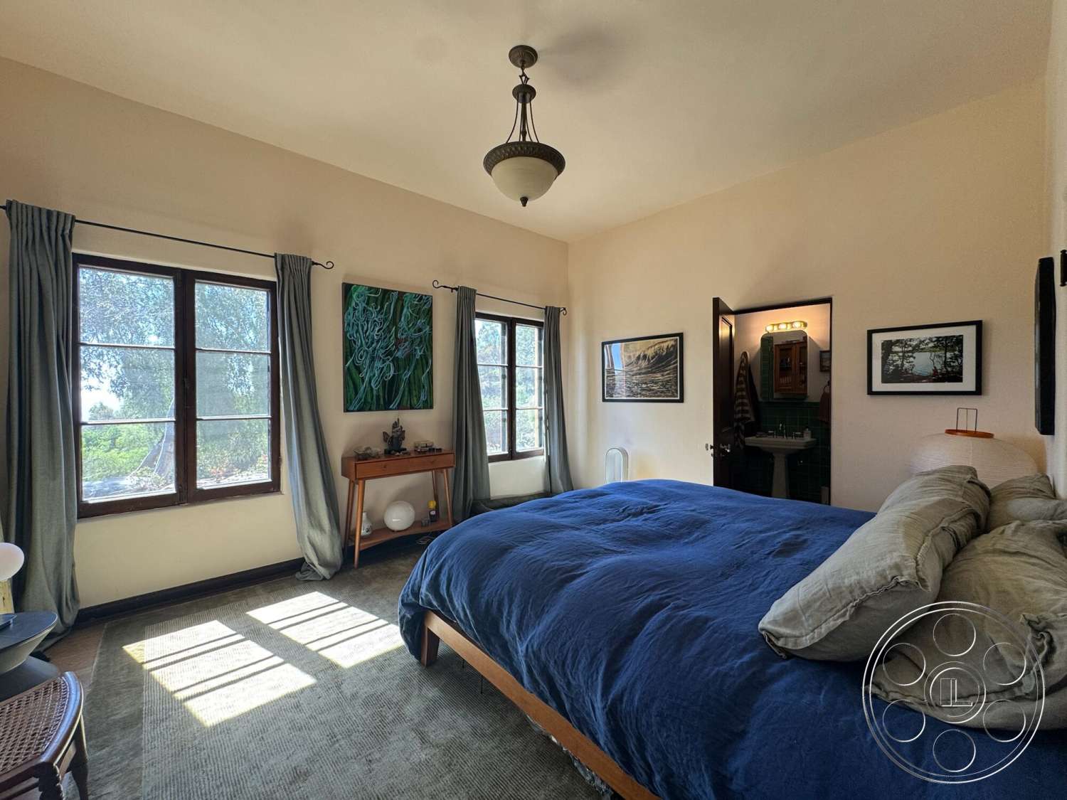 Farmstead Garden - floor-to-ceiling windows, wooden bed frame, wooden side table, hardwood bedroom floors, dark wood window frames, textured carpet flooring, artwork wall decor, light beige painted walls, open doorway to bathroom, traditional chandelier light fixture, draped window curtains, plush blue bedspread