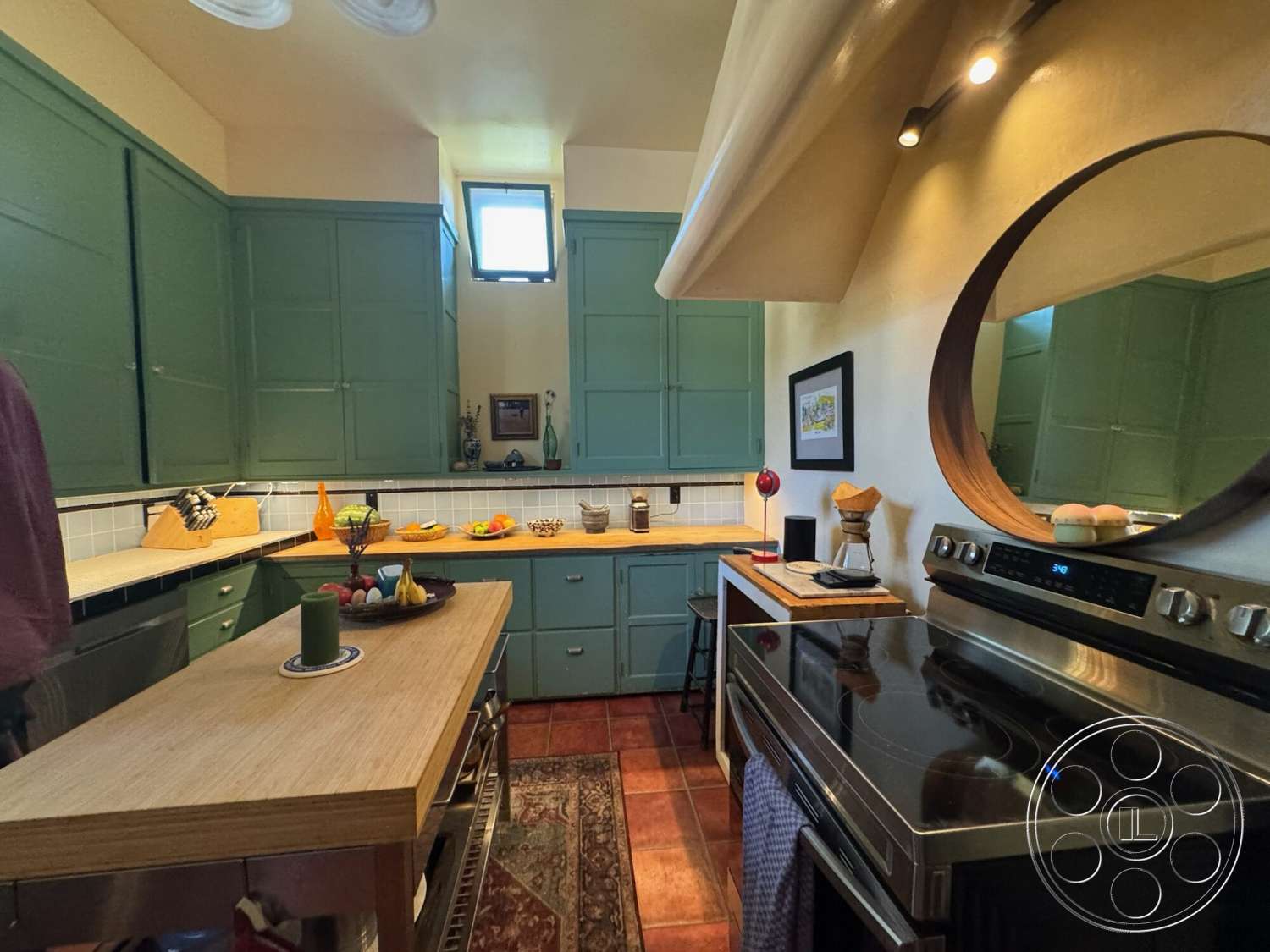 Farmstead Garden - stainless steel appliances, open shelving, framed wall art, under-cabinet lighting, interior kitchen, terra-cotta tile flooring, wood countertop island, round mirror with wooden frame, green painted cabinet doors, beige tile backsplash, red ceramic fruit bowl, kitchen utensil holder, decorative fruit display