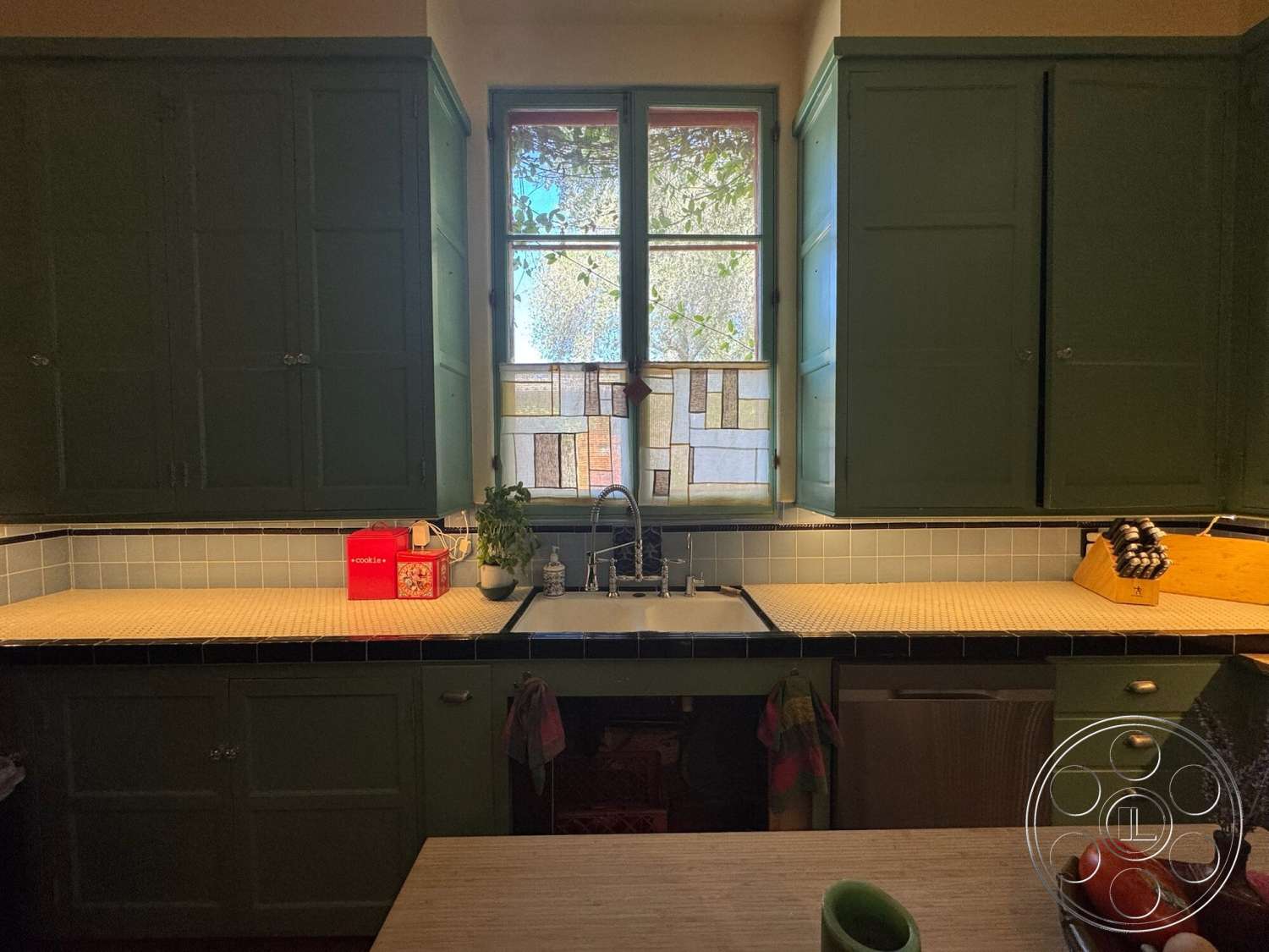 Farmstead Garden - natural light from window, green cabinetry, interior kitchen, white subway tile backsplash, double basin farmhouse sink, tile countertop, glass window with stained glass details, black accent trim, wooden knife block, kitchen utensils holder