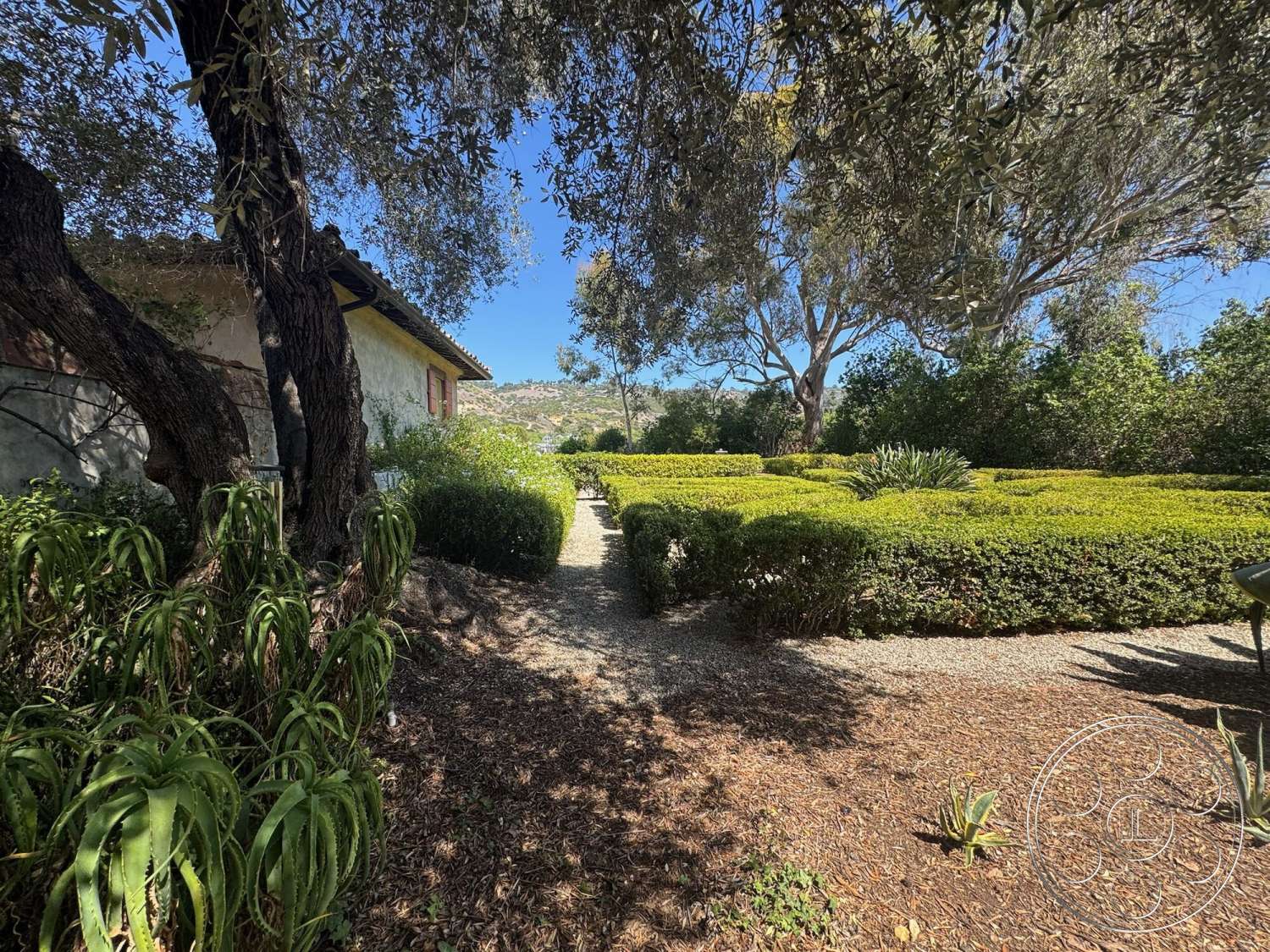 Farmstead Garden - exterior, outdoor seating area, gravel pathway, sunlit garden, tile roof, boxwood hedges, landscape greenery, Mediterranean architectural style, stucco wall finish, mature olive trees, vibrant garden setting, textured soil