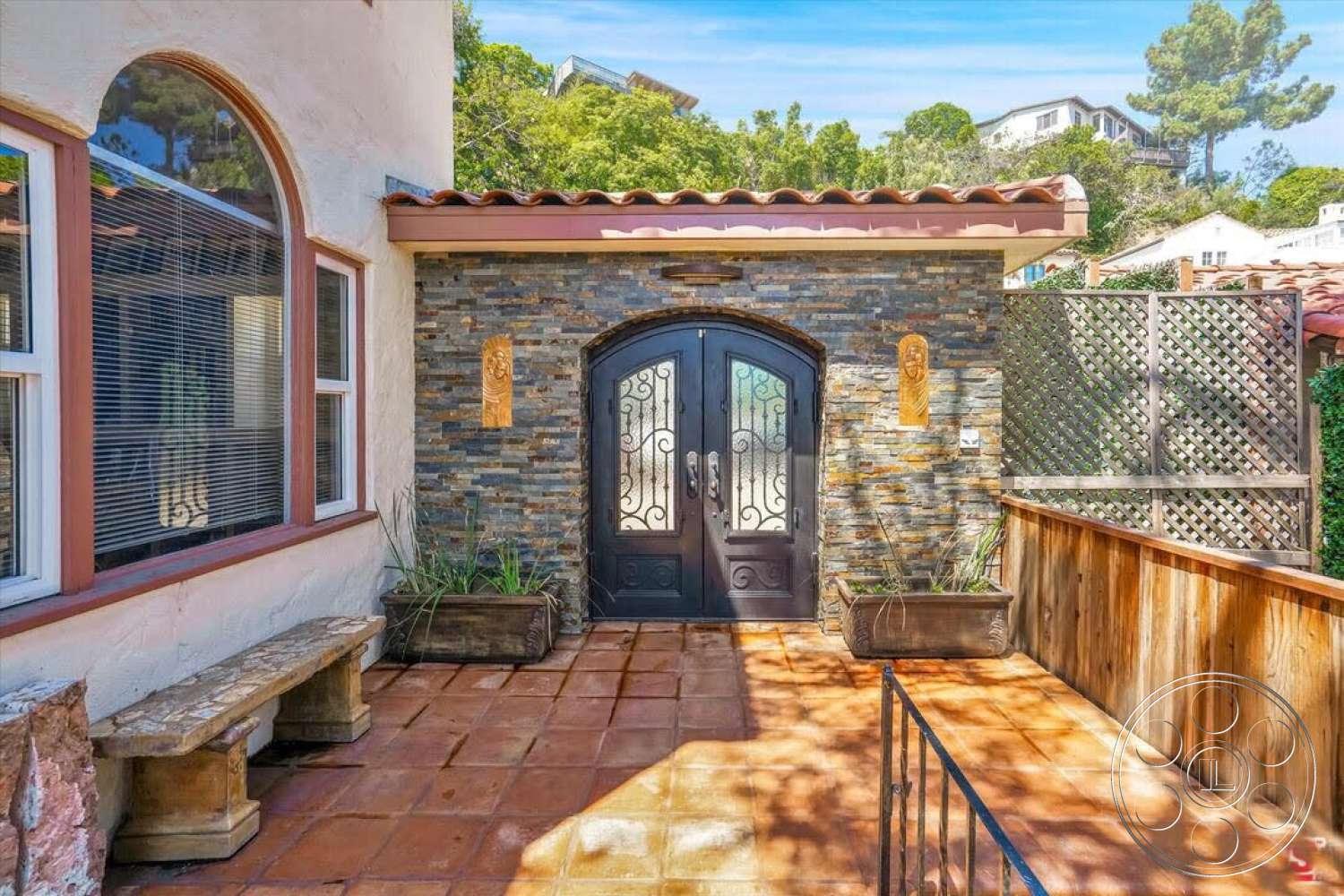 Spanish 170 - exterior, landscaped garden, planter boxes, light-colored stucco walls, arched entryway, wooden privacy fence, stone feature wall, natural stone accent, terracotta patio flooring, decorative wrought iron door, curved roof tiles