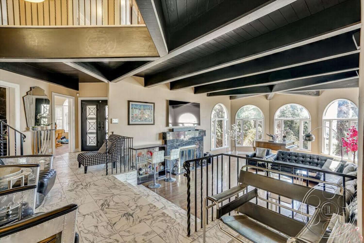 Spanish 170 - open floor plan, marble flooring, textured wall treatment, arched windows, black wood beam ceiling, stylish accent decor, glass partition railing, black and white plaid accent chair, polished stone fireplace, chic modern bar area