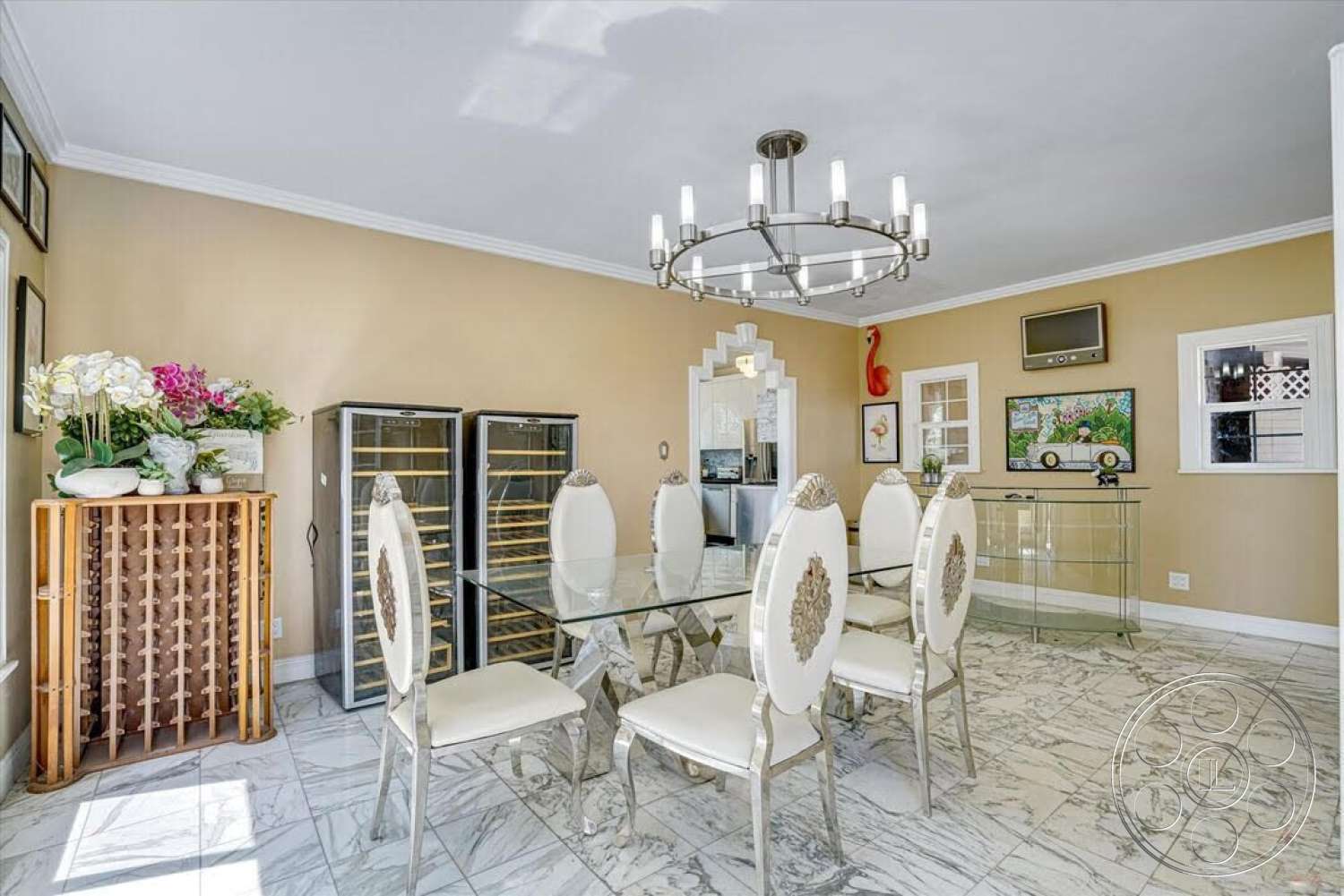 Spanish 170 - recessed lighting, glass dining table, decorative wall art, floral arrangements, glass display cabinet, tile backsplash, chrome chandelier, white painted walls, crown molding details, marble dining room flooring, wrought iron dining chairs, wooden wine rack