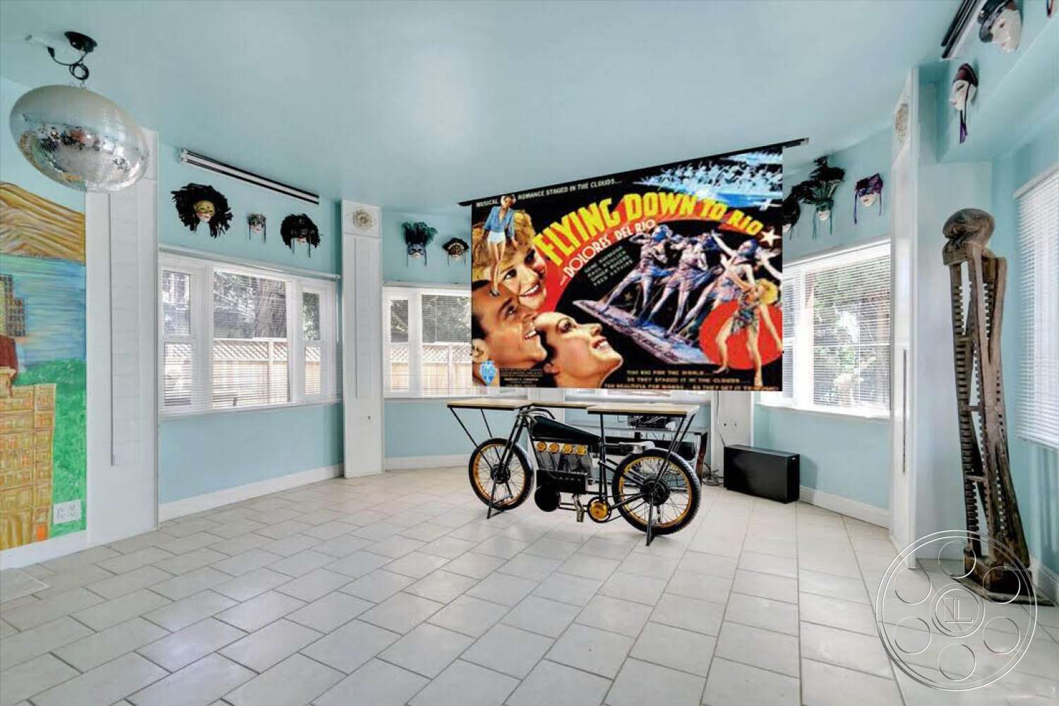 Spanish 170 - ceramic tile flooring, decorative sculptures, artistic wall murals, open layout space, large windows with blinds, multi-functional room, exposed ceiling light fixture, light blue painted walls, movie poster decor