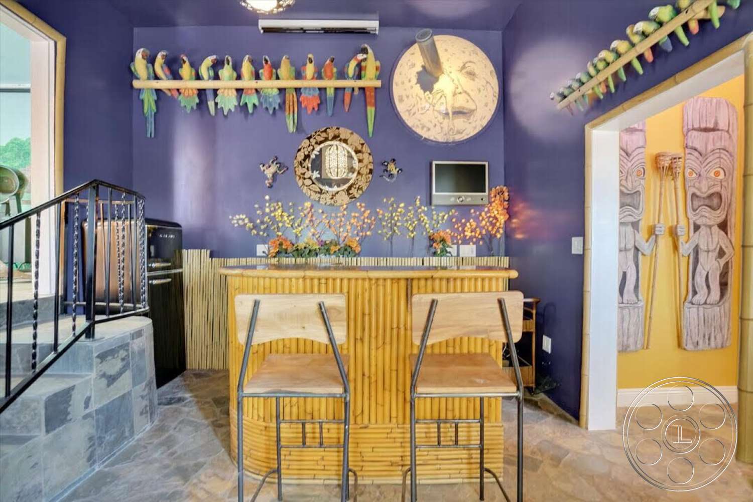 Spanish 170 - slate stone flooring, exposed ceiling, floral arrangement, modern lighting fixture, purple accent wall, black metal stair railing, bamboo bar stools, bamboo bar counter, decorative tiki carvings, colorful parrot wall decor, circular mirror decoration, small television mount