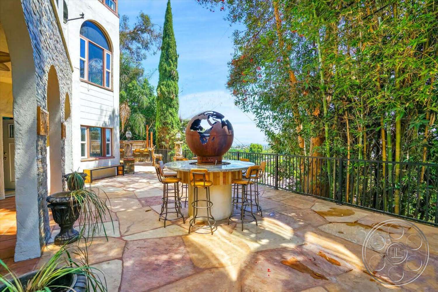 Spanish 170 - floor-to-ceiling windows, metal bar stools, tropical landscaping, outdoor setting, lush greenery backdrop, exposed stone wall, natural stone patio flooring, interior arched doorways, wood beam construction, wooden table with globe centerpiece