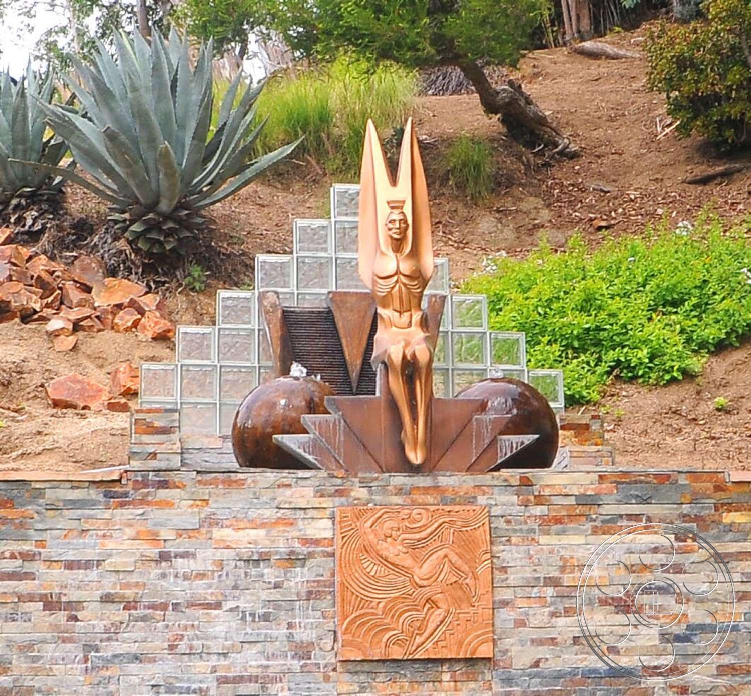 Spanish 170 - exterior, textured stone tiles, glass block wall, lush green landscaping, tropical plant surroundings, natural stone landscaping, stacked stone feature wall, bronze sculpture fountain, geometric fountain design, decorative relief panel, curved boulders