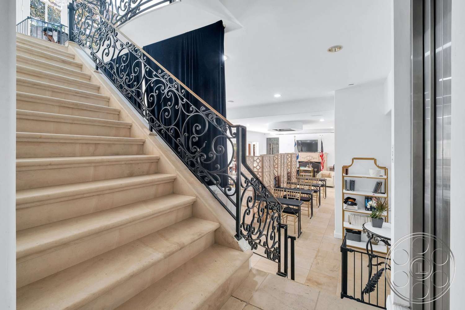 French 29 - recessed ceiling lights, decorative wrought iron railing, open floor plan living area, neutral-colored walls, interior staircase with beige limestone steps, tile flooring in living and dining space, modern elevator entrance, expansive view from the staircase, contemporary furniture setup in living area