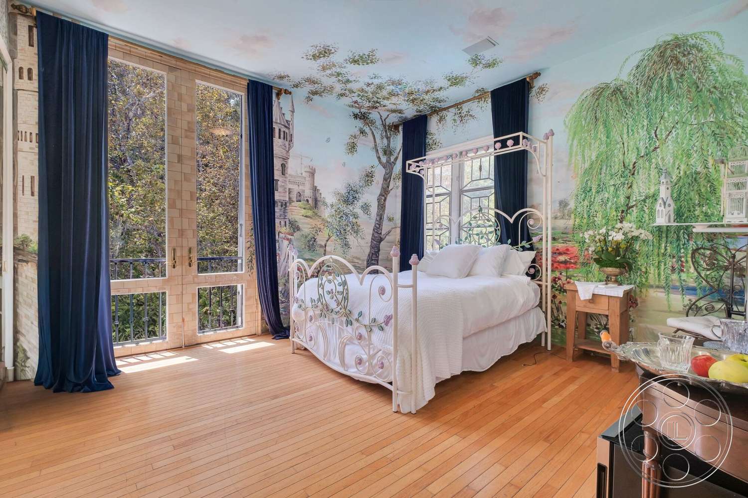 French 29 - natural light, floral decor, white quilted bedding, hardwood bedroom floors, small wooden side table, double glass doors, wrought iron balcony railings, iron canopy bed, blue velvet curtains, accent wall with mural, decorative silver tray