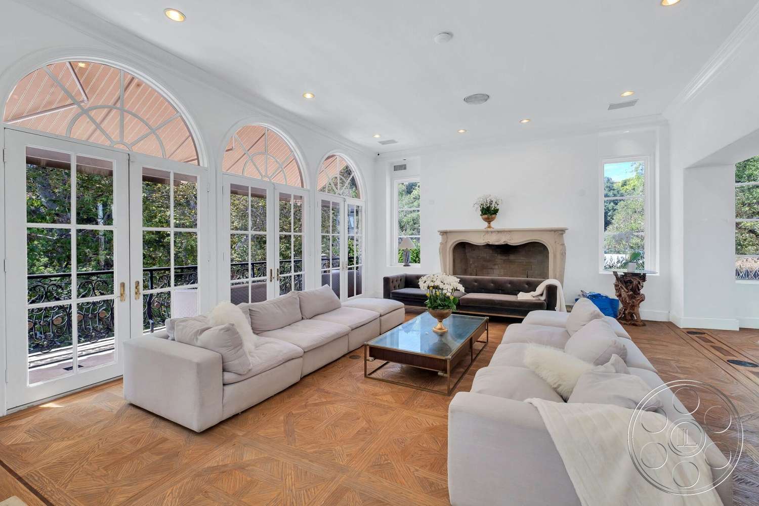 French 29 - minimalist decor, open floor plan, natural light from large windows, arched windows, rectangular coffee table, white painted walls, modern sectional sofa, decorative indoor plants, stone fireplace surround, elegant chandelier lighting, wooden floor with herringbone pattern