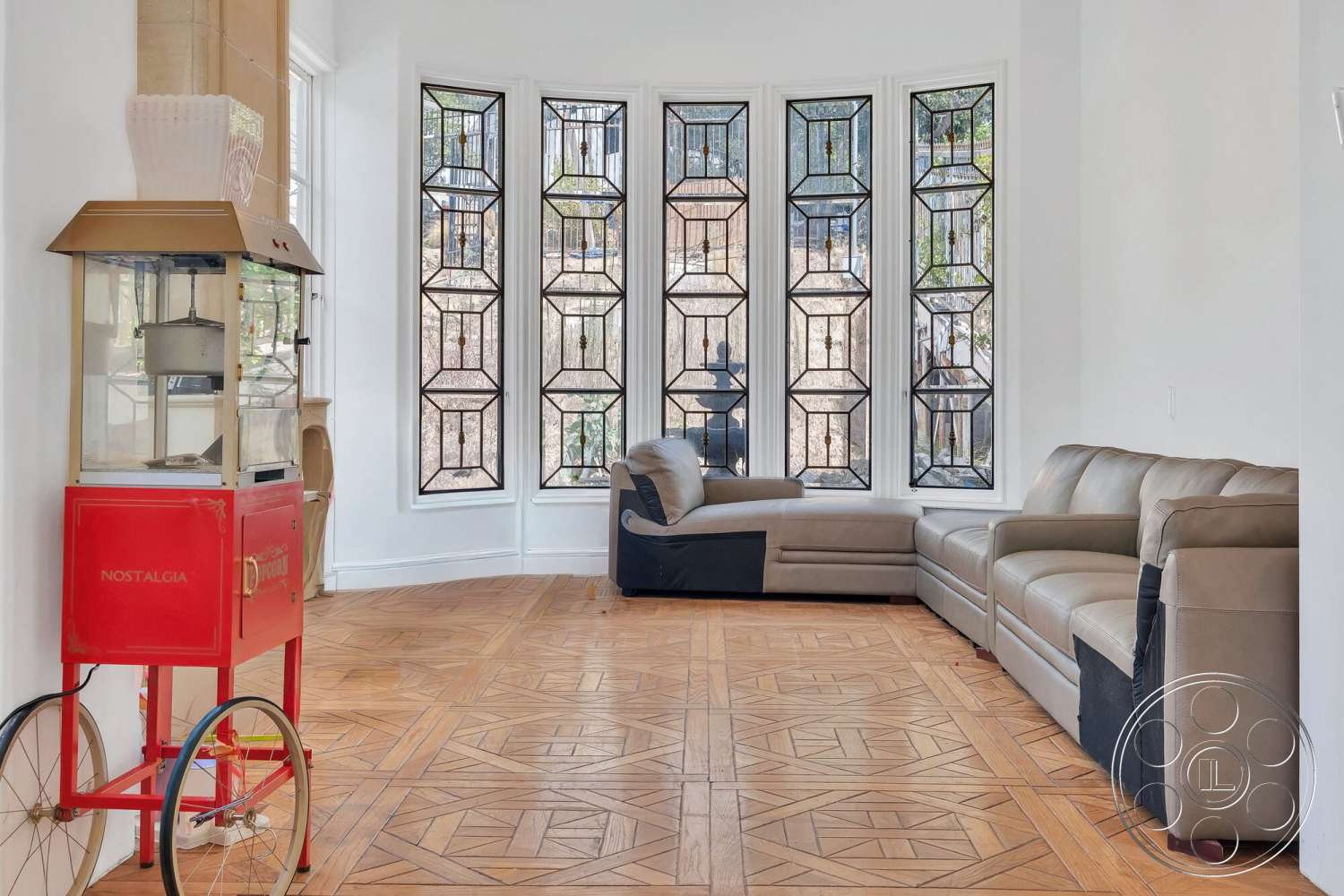 French 29 - natural light, stained glass windows, open living space, bright white walls, modern sectional couch, bay window design, hardwood flooring with geometric pattern, vintage style popcorn machine