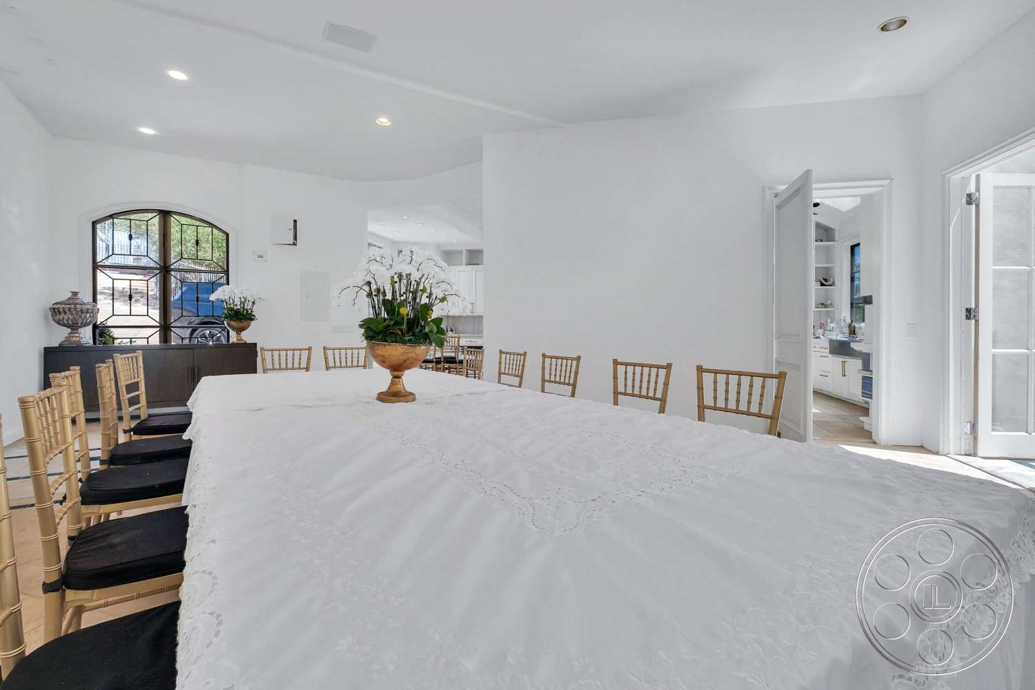 French 29 - minimalist decor, natural light from windows, rectangular dining table, white painted walls, hardwood dining room floors, linen tablecloth, golden bamboo chairs, arched window with decorative grille, potted orchids as centerpiece, open doorway leading to kitchen
