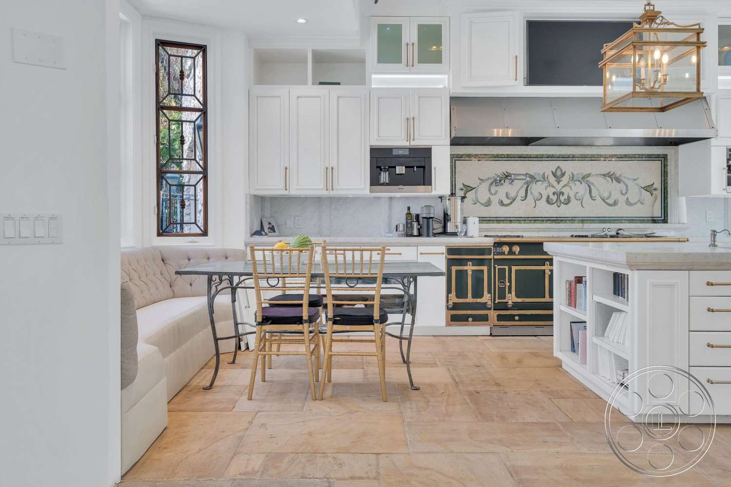 French 29 - exterior, floor-to-ceiling windows, decorative wall art, cozy breakfast nook, marble kitchen backsplash, white painted walls, cream-colored stone flooring, modern kitchen area, golden pendant light fixture, green vintage stove, custom built-in white kitchen cabinets, tufted upholstery bench seating, round metal dining table