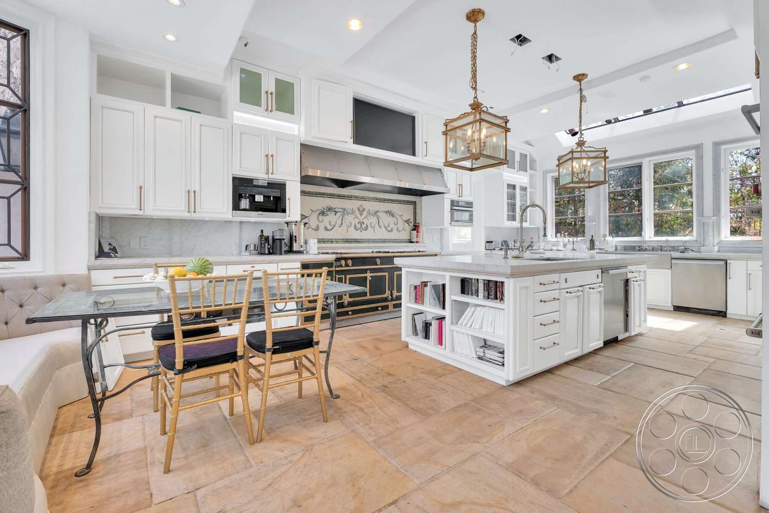 French 29 - stainless steel kitchen appliances, marble countertop island, exposed ceiling with recessed lighting, open-plan kitchen layout, white shaker kitchen cabinets, square dining table, gold pendant lighting fixtures, window view of garden, handcrafted tile backsplash, beige stone tile flooring, upholstered corner bench seating, golden wooden dining chairs, decorative wall niche with artwork