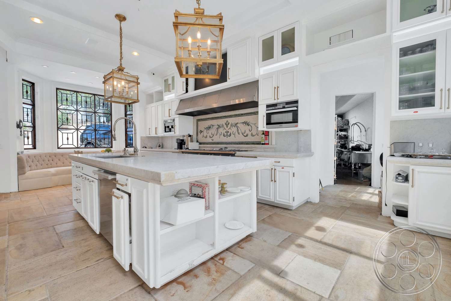 French 29 - stainless steel appliances, exposed wood ceiling beams, interior kitchen, marble kitchen island countertop, spacious cooking area, open floor layout, built-in kitchen storage, white shaker-style kitchen cabinets, stone backsplash with decorative design, tan stone tile flooring, hanging glass lantern light fixtures, floor-to-ceiling decorative windows