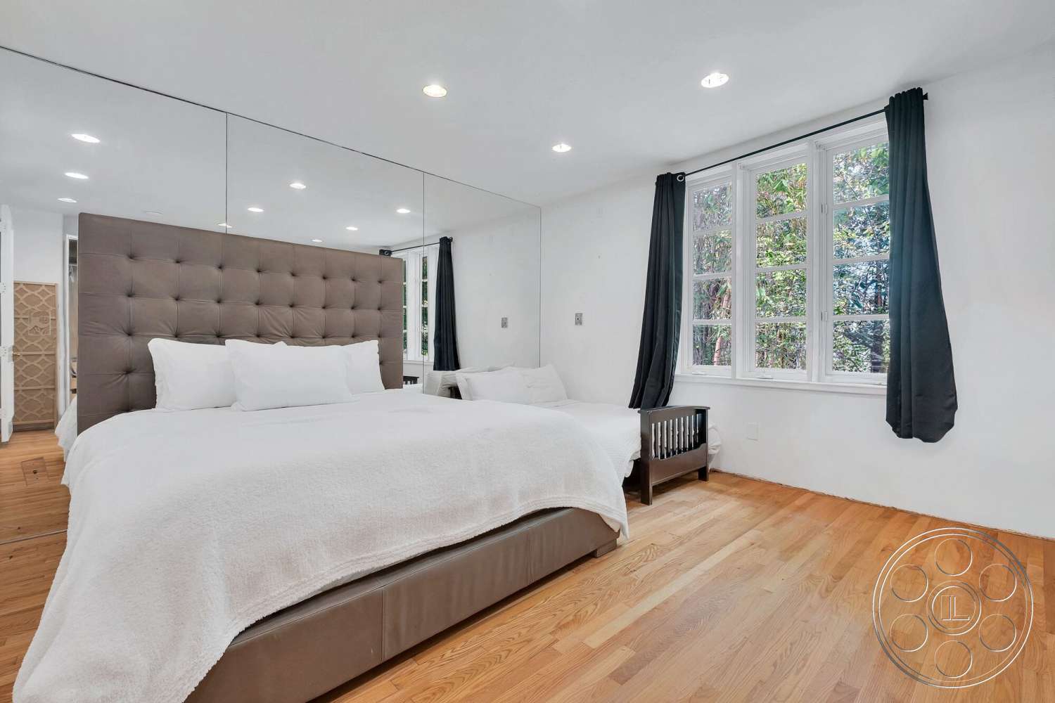 French 29 - floor-to-ceiling windows, white bedding, minimalist interior design, hardwood bedroom floors, neutral painted walls, modern bedside table, light fixture recessed lighting, upholstered headboard bed, mirrored accent wall, black curtain drapes
