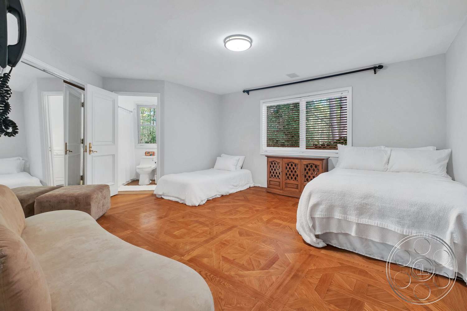 French 29 - floor-to-ceiling windows, white painted walls, parquet wood bedroom flooring, two twin beds with white bedding, brown upholstered sofa chair, wood storage cabinet