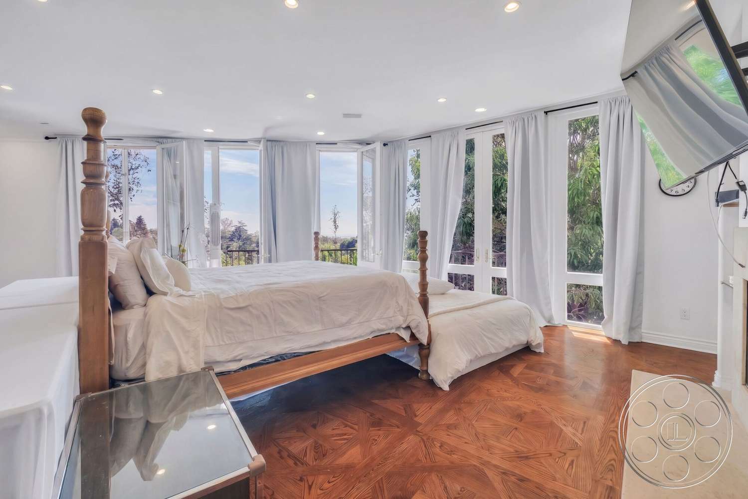 French 29 - floor-to-ceiling windows, bright natural lighting, hardwood bedroom floors, white painted walls, modern wall-mounted television, minimalist design features, queen-size bed with wooden posts, lightweight fabric curtains, elegant bed linens, calming interior setting