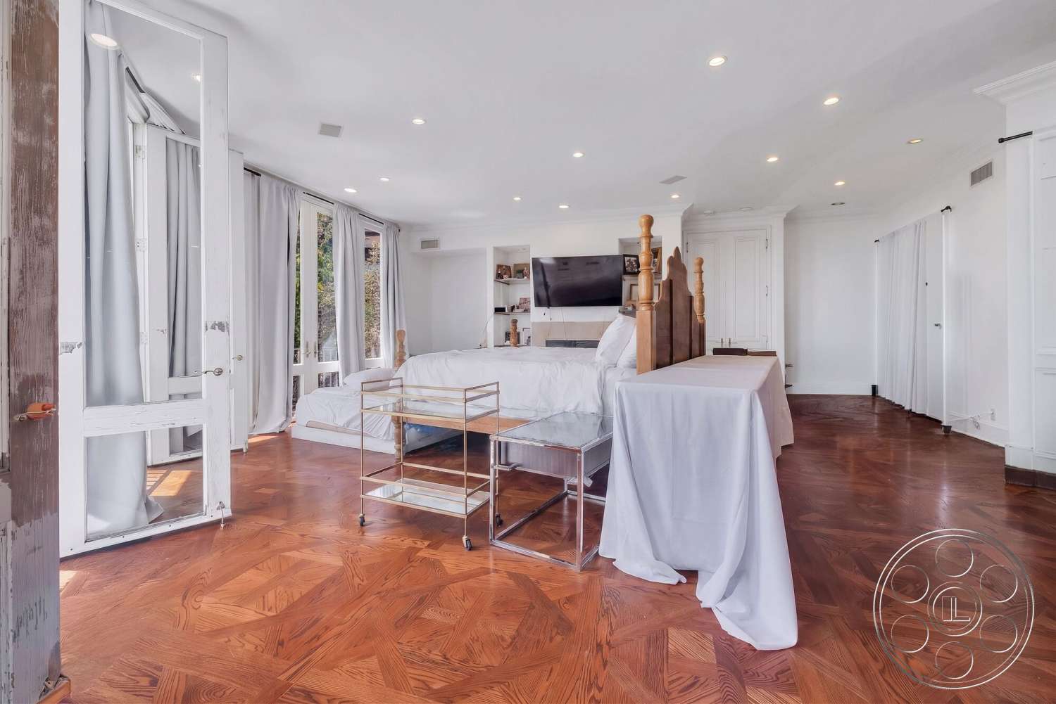 French 29 - built-in cabinetry, recessed ceiling lighting, white painted walls, wood herringbone flooring, large windows with greenery view, modern glass coffee table, exposed wooden door frame, flat-screen television wall mount, light gray drapery, queen-sized bed with wooden headboard