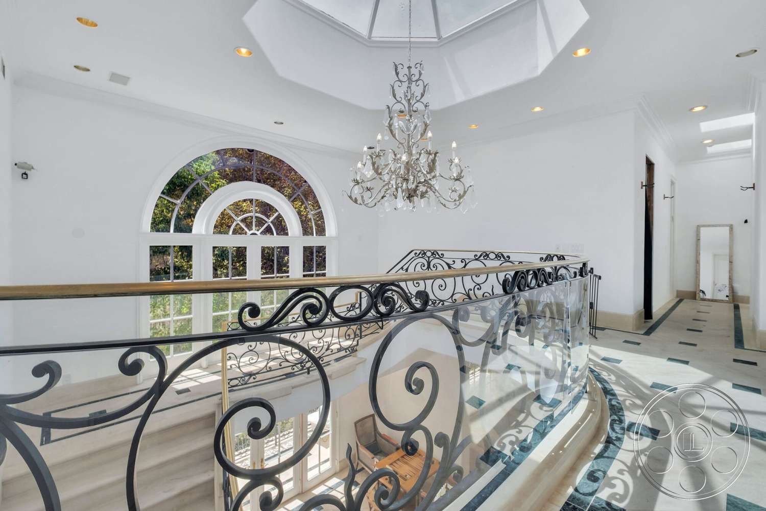 French 29 - high vaulted ceiling, decorative crown molding, large arched windows, dark wood door, natural light illumination, white painted walls, skylight ceiling, chandelier with crystal accents, open hallway design, intricate wrought iron railing, marble flooring with decorative inlays