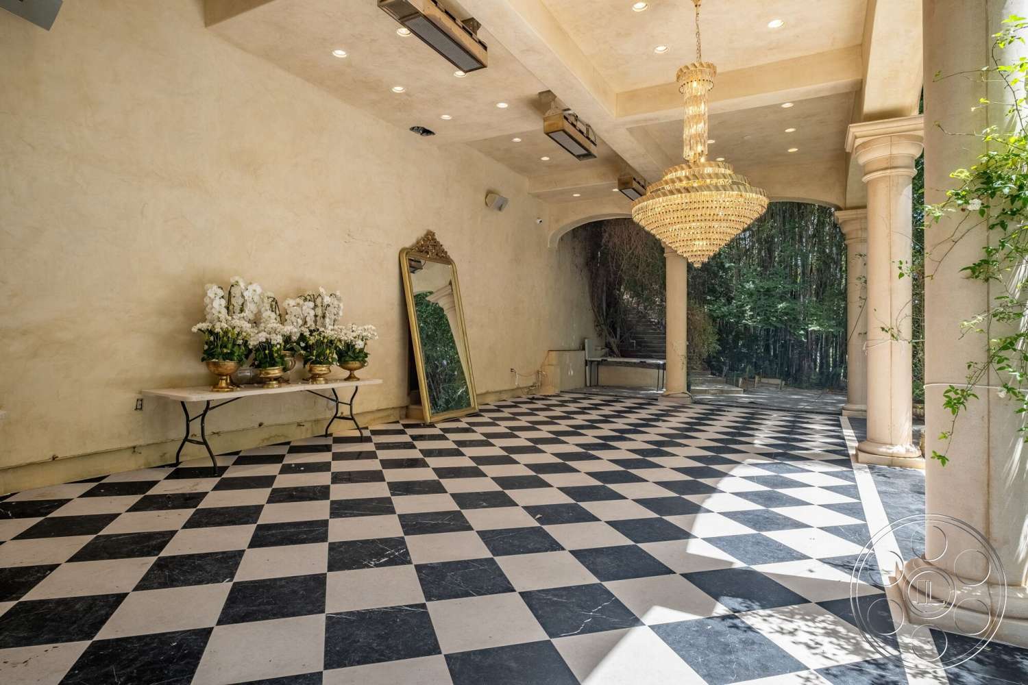 French 29 - open space layout, natural greenery view, textured plaster walls, decorative floral arrangements, chandelier lighting fixture, large wall mirror, exposed column details, marble checkered flooring