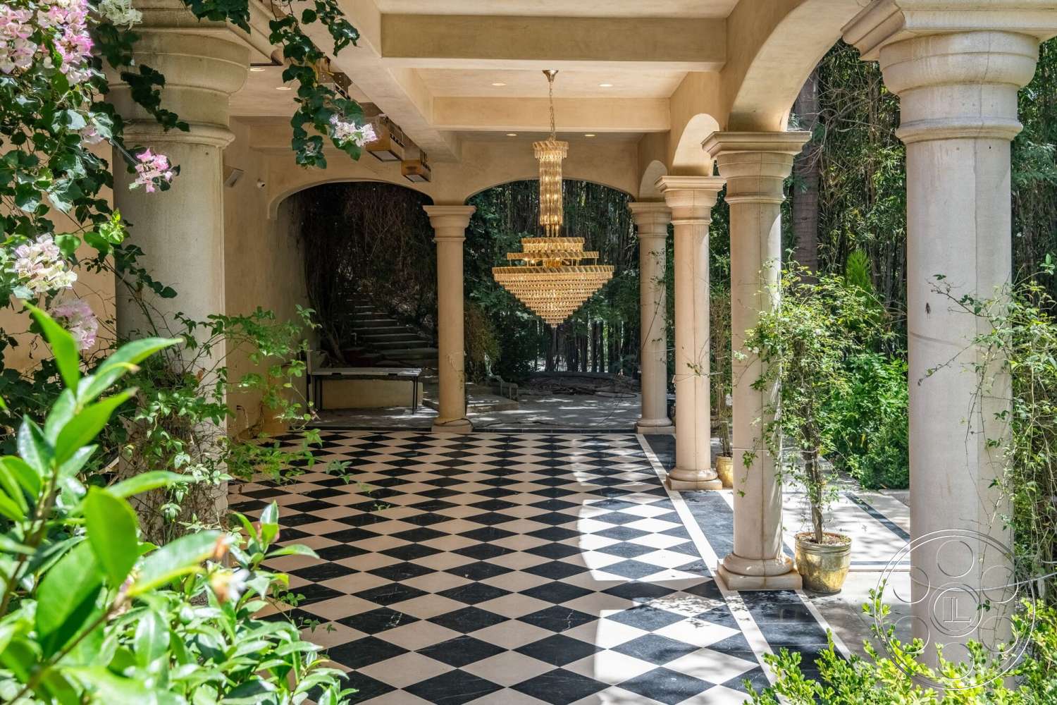French 29 - exterior, lush greenery, string lights, textured plaster ceiling, outdoor staircase, chandelier lighting fixture, decorative flower arrangements, open-air walkway, polished concrete columns, checkered tile patio flooring, framed archways, symmetrical column arrangement