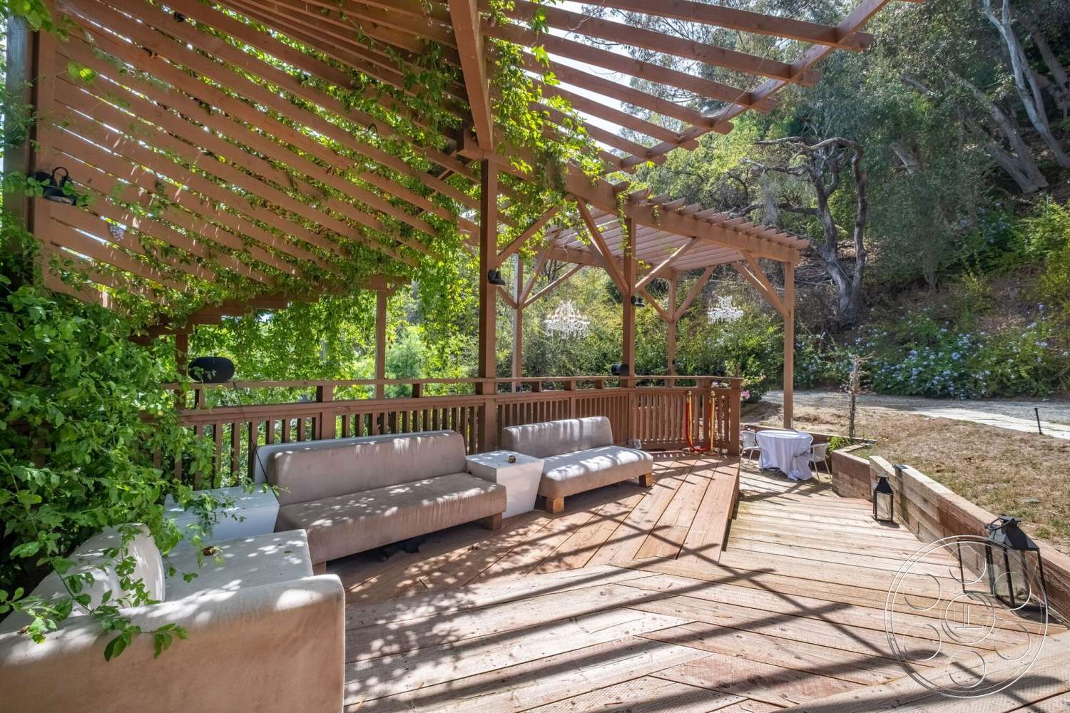 French 29 - exterior, upholstered outdoor seating, wooden deck flooring, wood pergola structure, open-air lounge area, integrated planters with greenery, ornamental lighting fixtures, mountainous garden setting