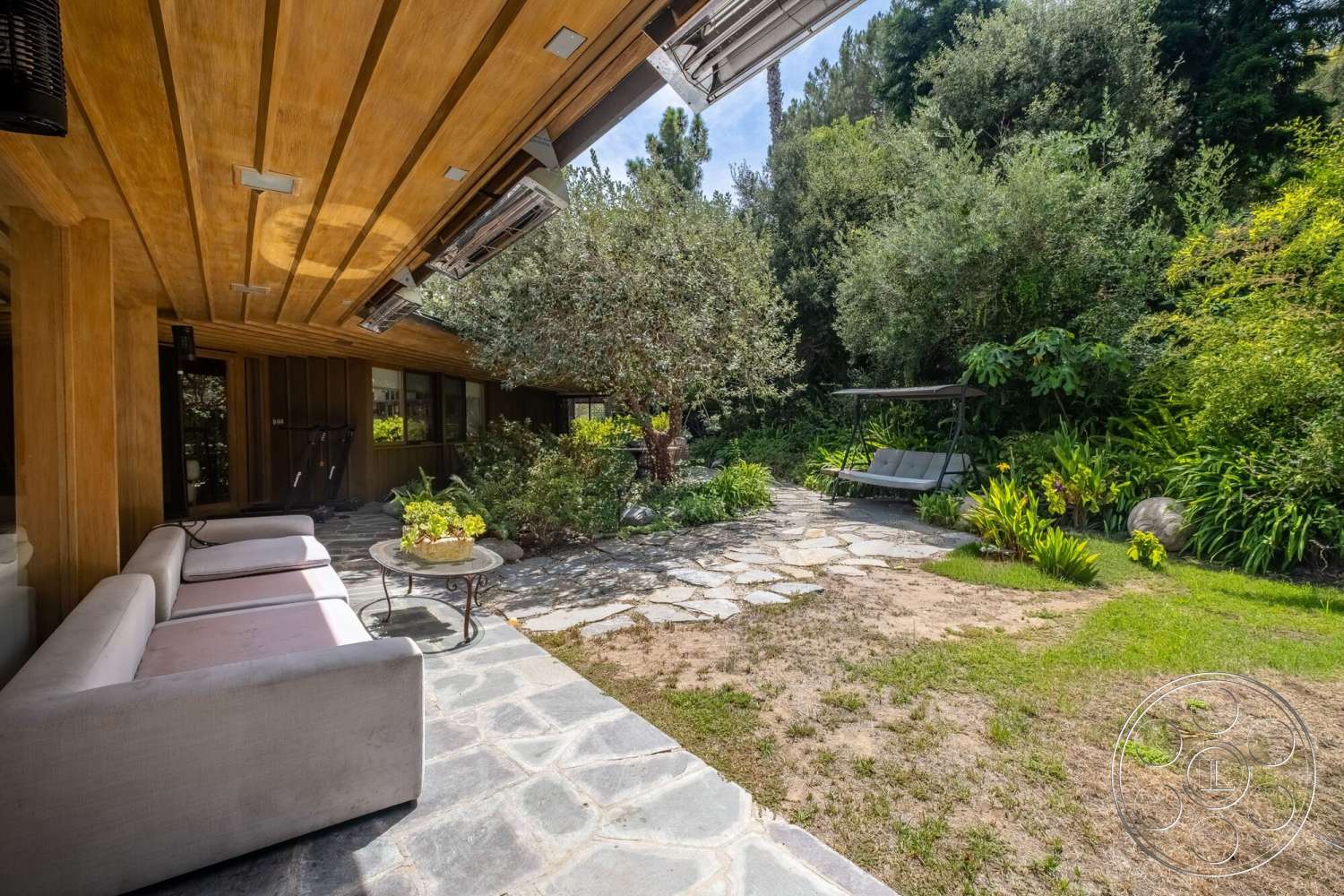 French 29 - exterior, glass sliding doors, natural stone pathway, wood ceiling beams, sustainable landscaping, modern outdoor seating, landscaped garden area, stone patio flooring, lush greenery surrounding, concrete patio floor, circular outdoor coffee table, exposed wood siding, linear garden layout, hammock swing