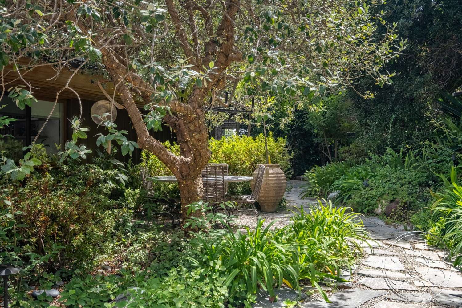 French 29 - exterior, outdoor dining area, garden setting, natural stone pathway, wooden patio furniture, lush green landscaping, sun-drenched outdoor space, overhanging tree branches, modern home exterior, stone garden accents, decorative ceramic planter, low shrubbery