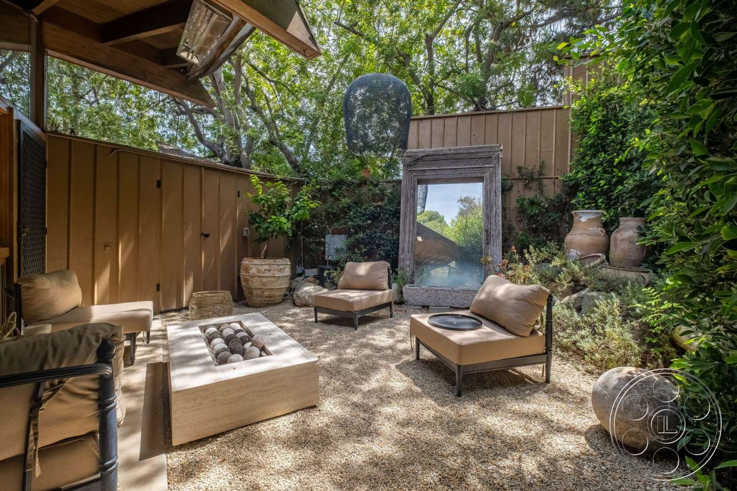 French 29 - exterior, relaxation area, natural setting, textured wall treatment, wooden privacy fence, modern seating area, wood beam ceiling, gravel patio flooring, concrete fire pit, landscaped garden with plants, outdoor decorative mirror, clay pottery planters