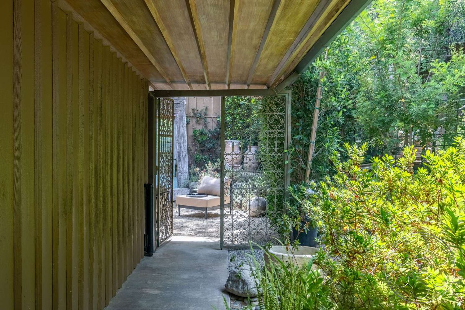 French 29 - landscaped garden, potted plants, wood panel ceiling, modern outdoor furniture, iron gate, textured wall panels, concrete path, vegetation border, exterior walkway, gravel patio area, leafy green surroundings