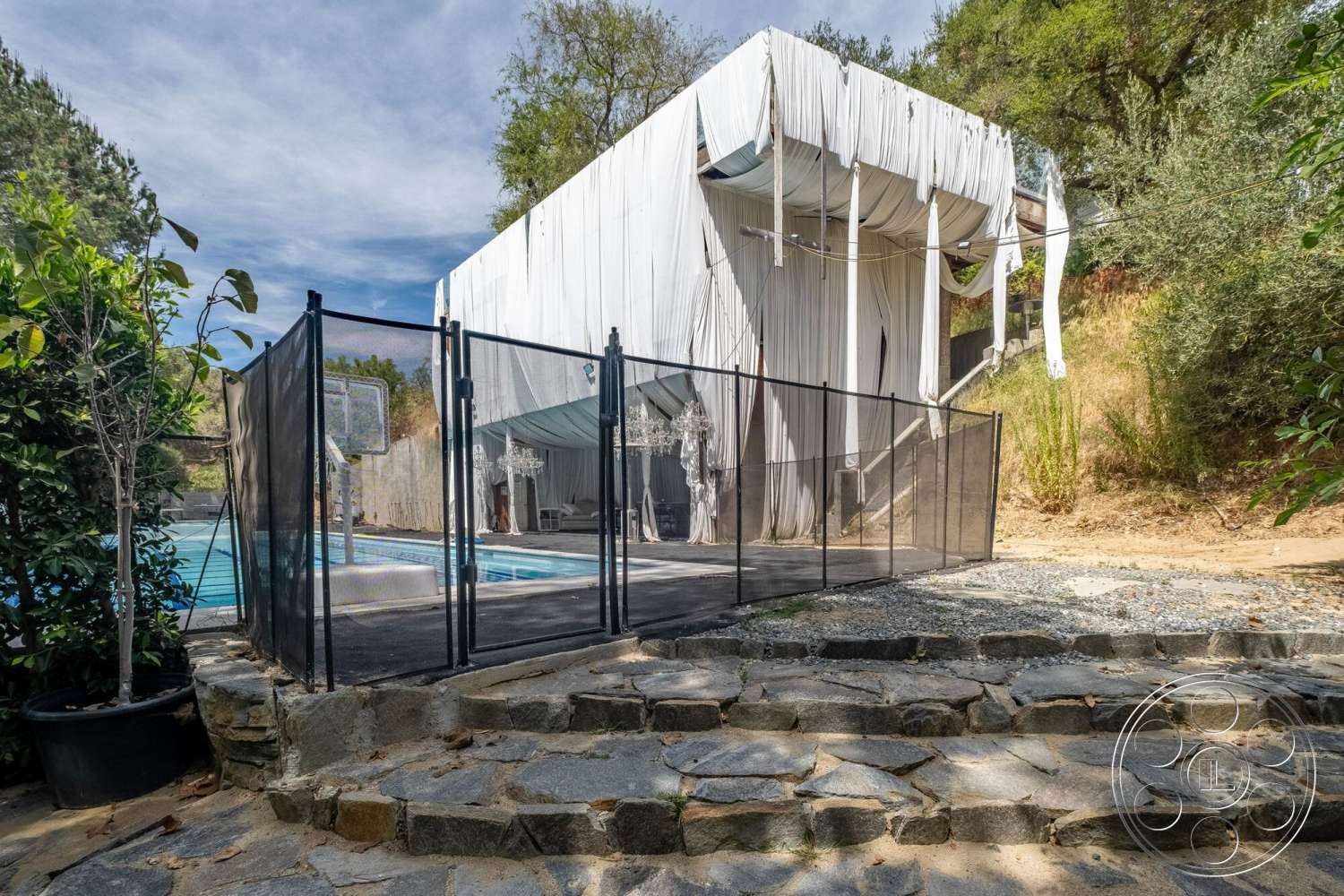 French 29 - exterior, landscaped garden, modern architecture, outdoor seating area, sloped terrain, rectangular swimming pool, glass windows, open-air design, concrete pool deck, ambient lighting fixtures, steel structural elements, natural hillside setting, textured fabric facade, stone patio steps, black mesh pool fence