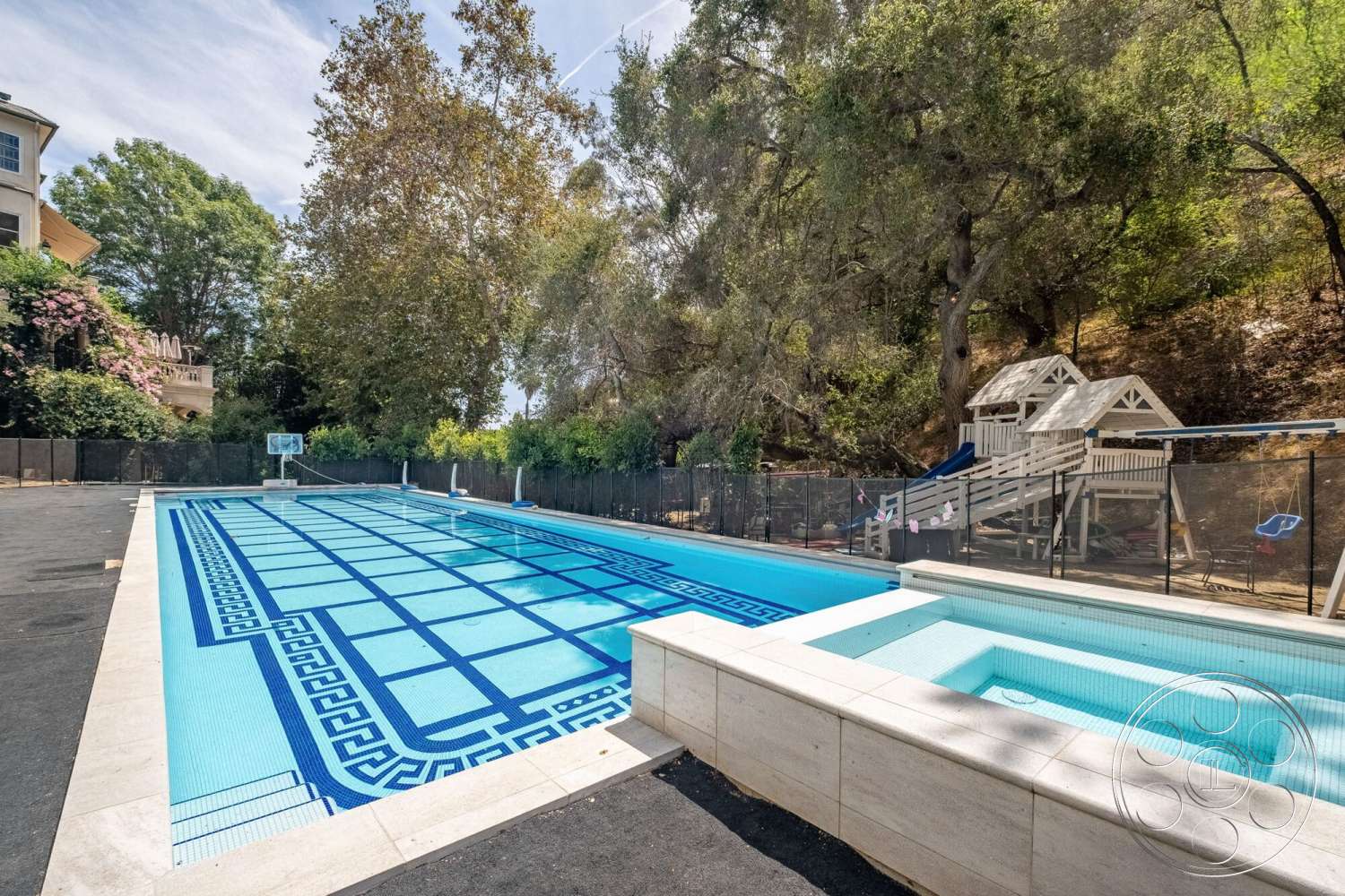 French 29 - exterior, rectangular swimming pool, concrete pool deck, concrete pool border, surrounding trees and greenery, tile pool flooring, fenced pool area, blue mosaic tile pattern, spa area with integrated hot tub, natural hillside landscaping, play structure with slide